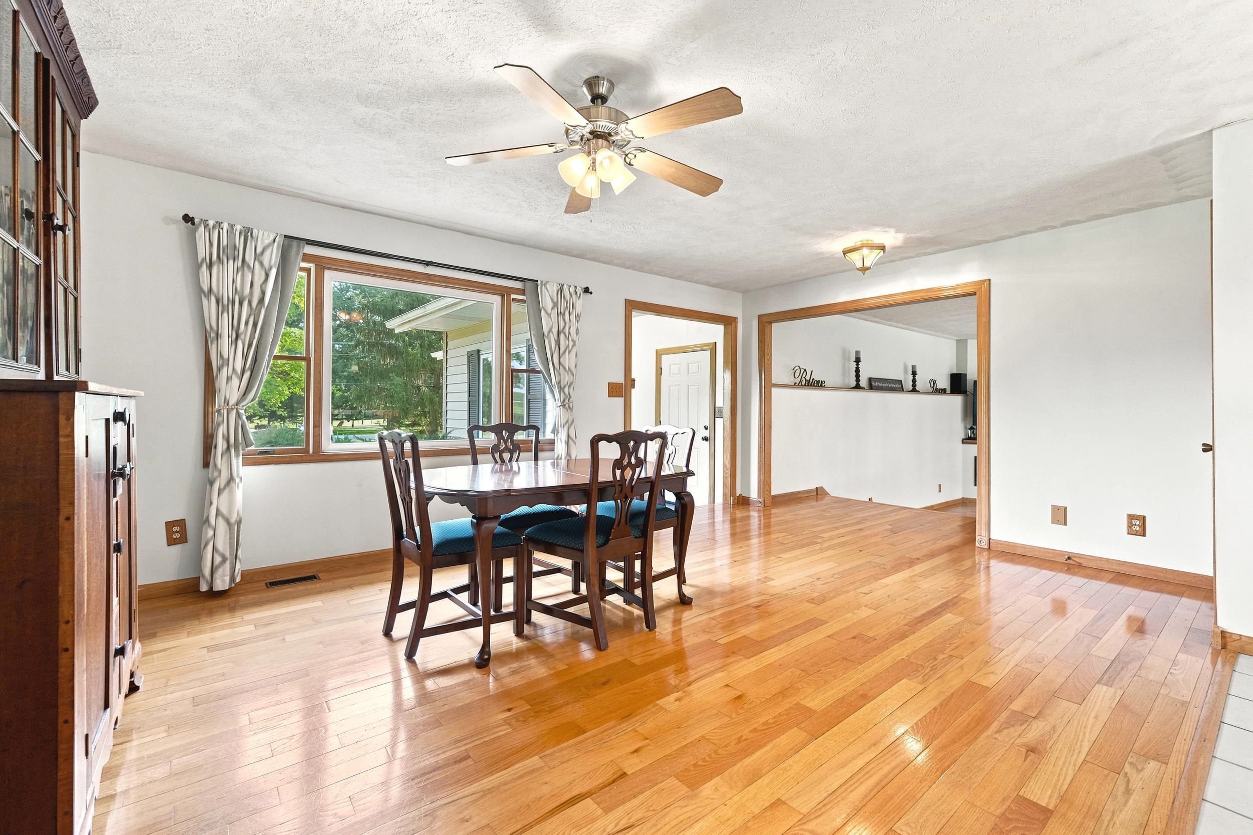 Open-concept dining area featuring wood-finish flooring, a large picture window, and a ceiling fan with integrated lighting