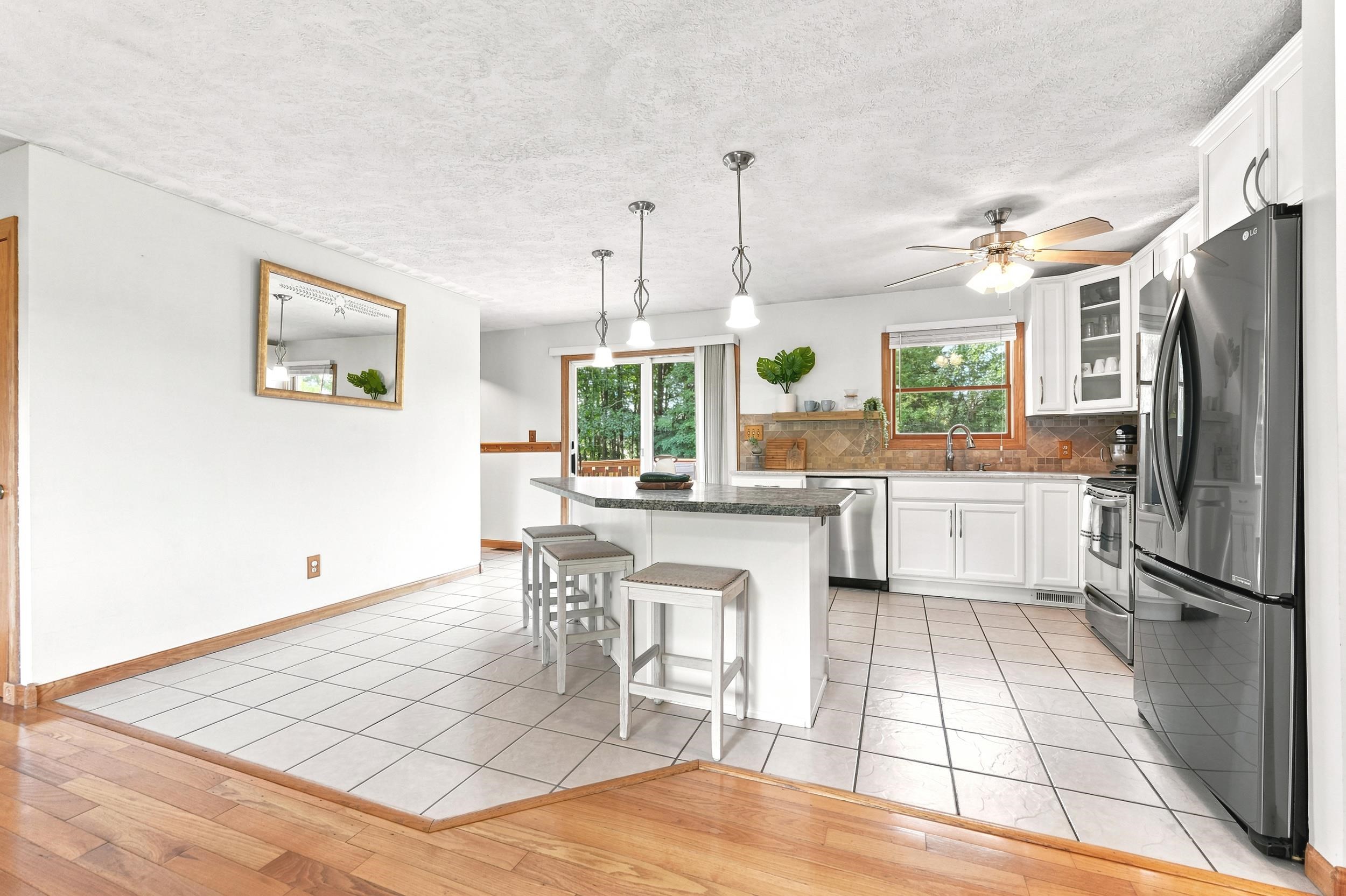 Contemporary kitchen featuring a center island with pendant lighting, white cabinetry, stainless steel appliances, and a stone-finish backsplash
