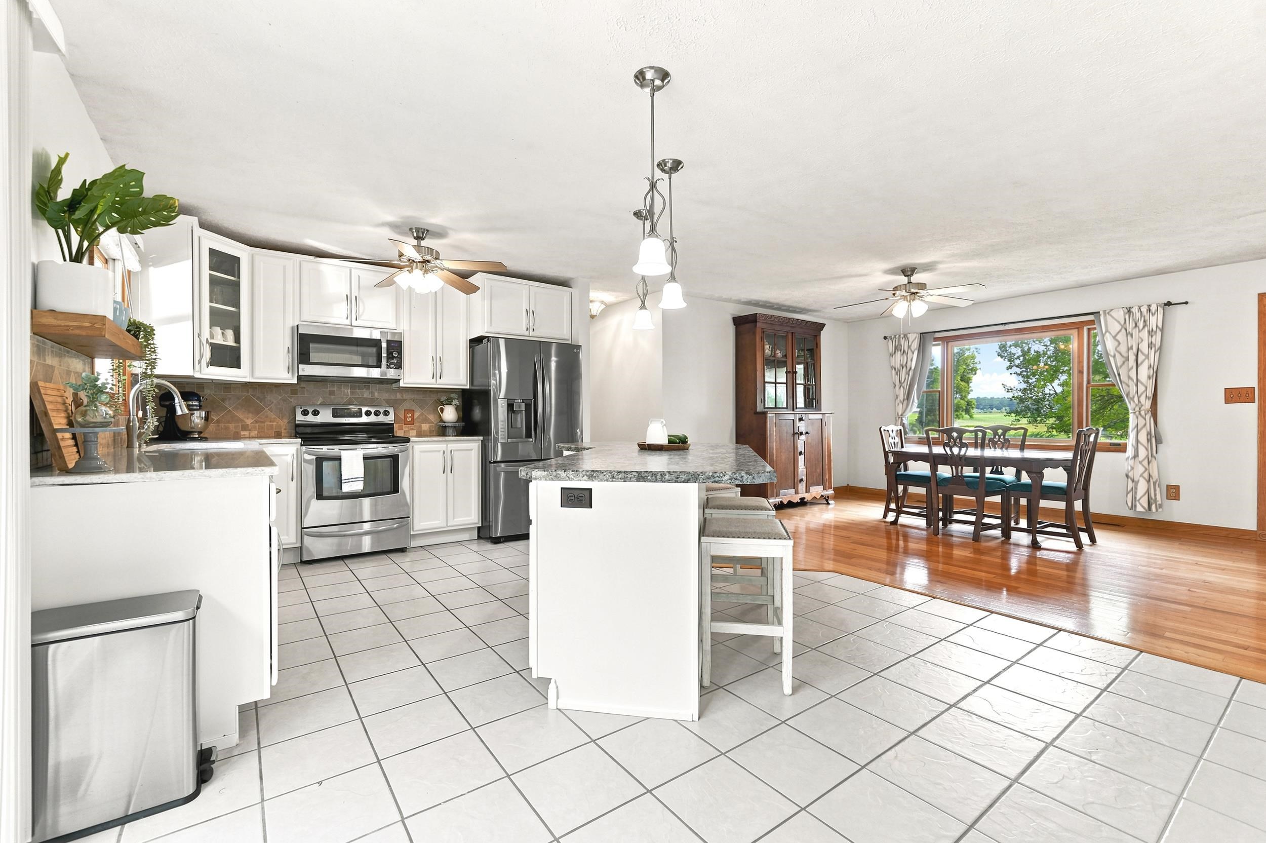 Open-concept kitchen featuring white cabinetry, stainless steel appliances, a central island with bar seating, and granite countertops