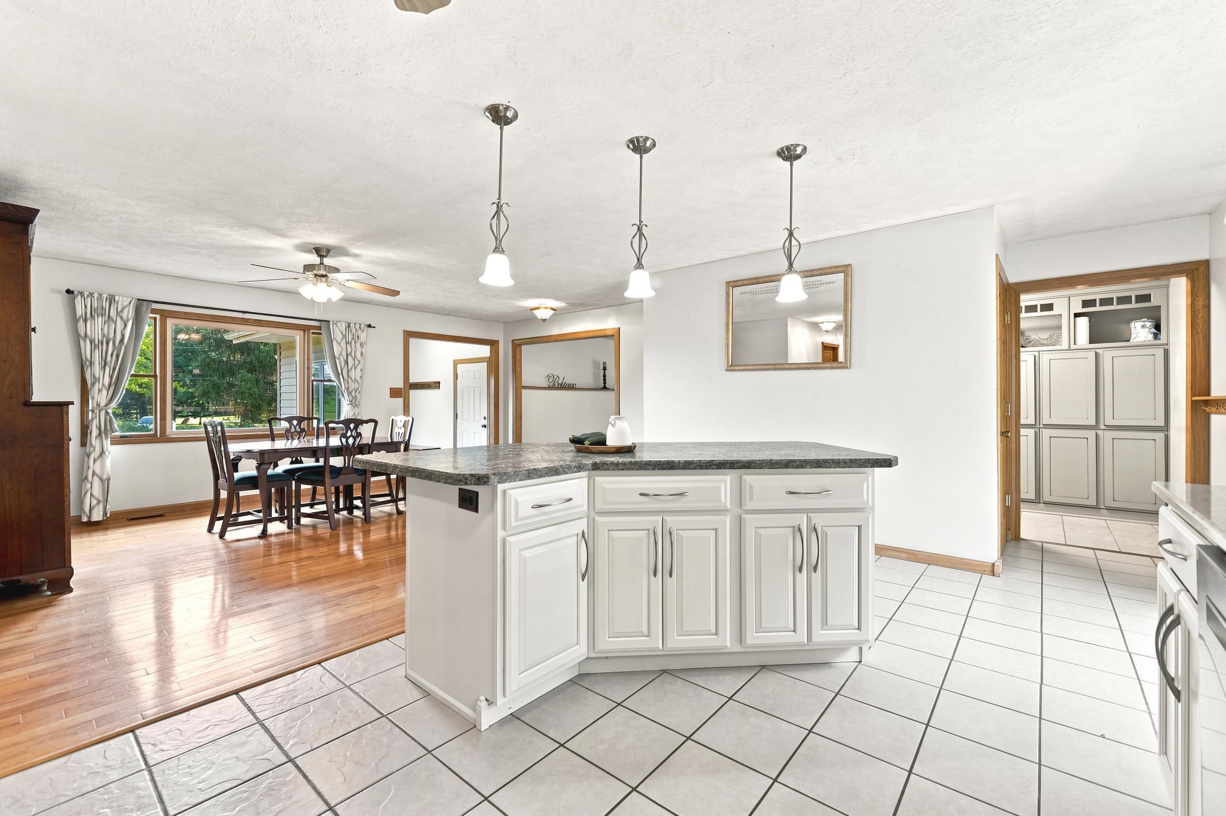 Kitchen island featuring white cabinetry, a dark countertop, and three pendant lights