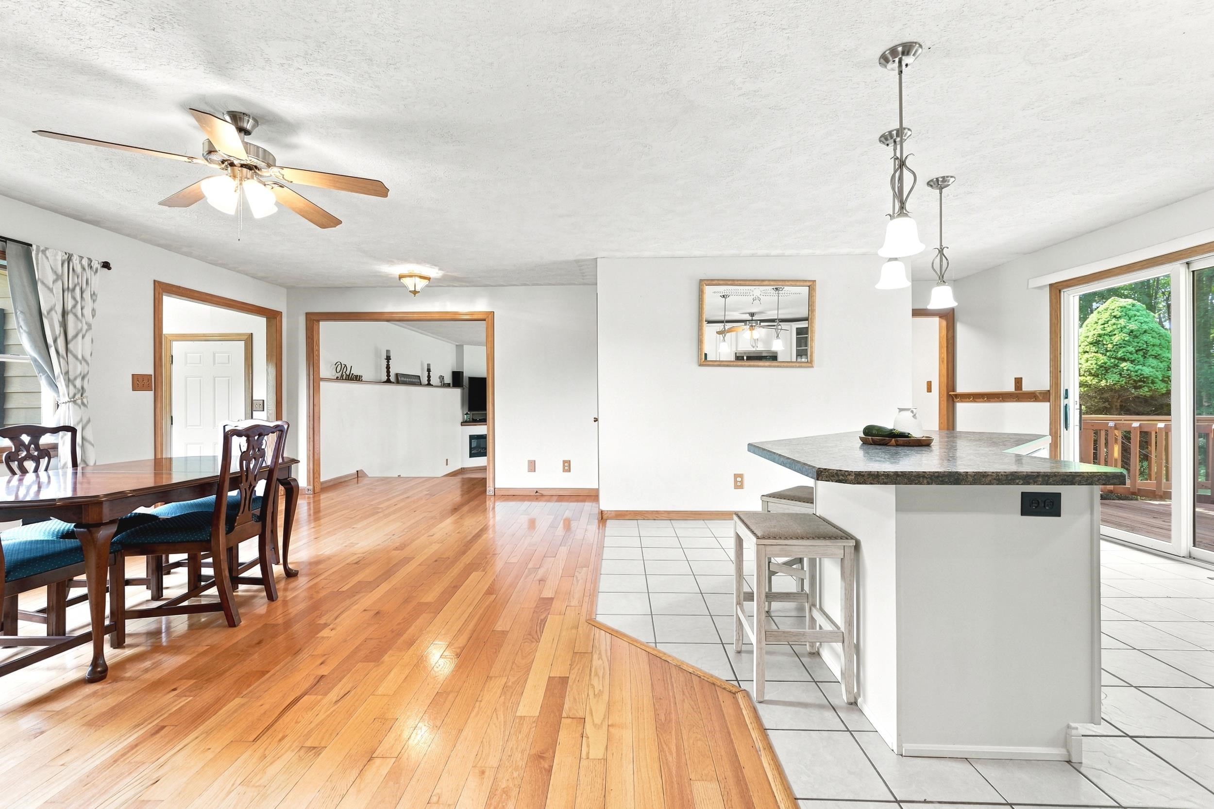Open-concept interior featuring wood-finish flooring, a kitchen island with a stone-finish countertop, white tile flooring, and a sliding glass door leading to an outdoor deck