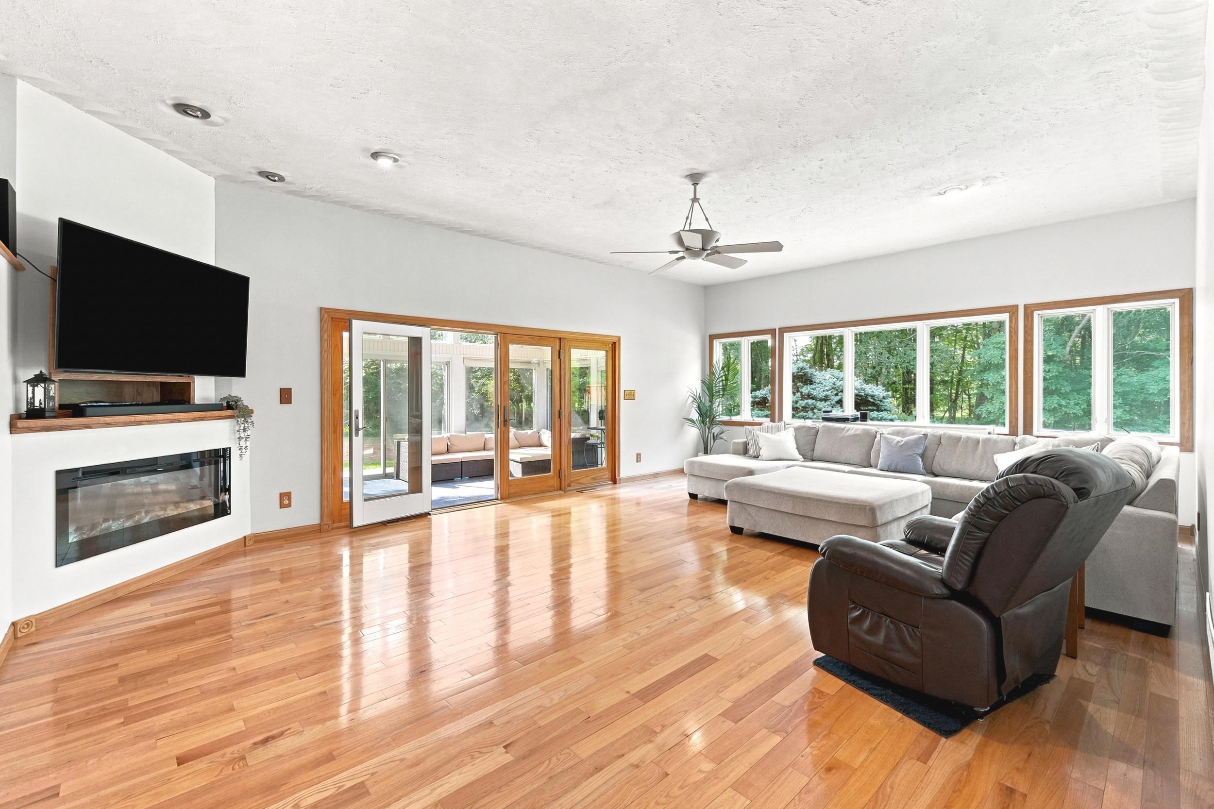 Spacious living area featuring polished wood flooring, a built-in electric fireplace with a wood mantle, recessed lighting, and a ceiling fan