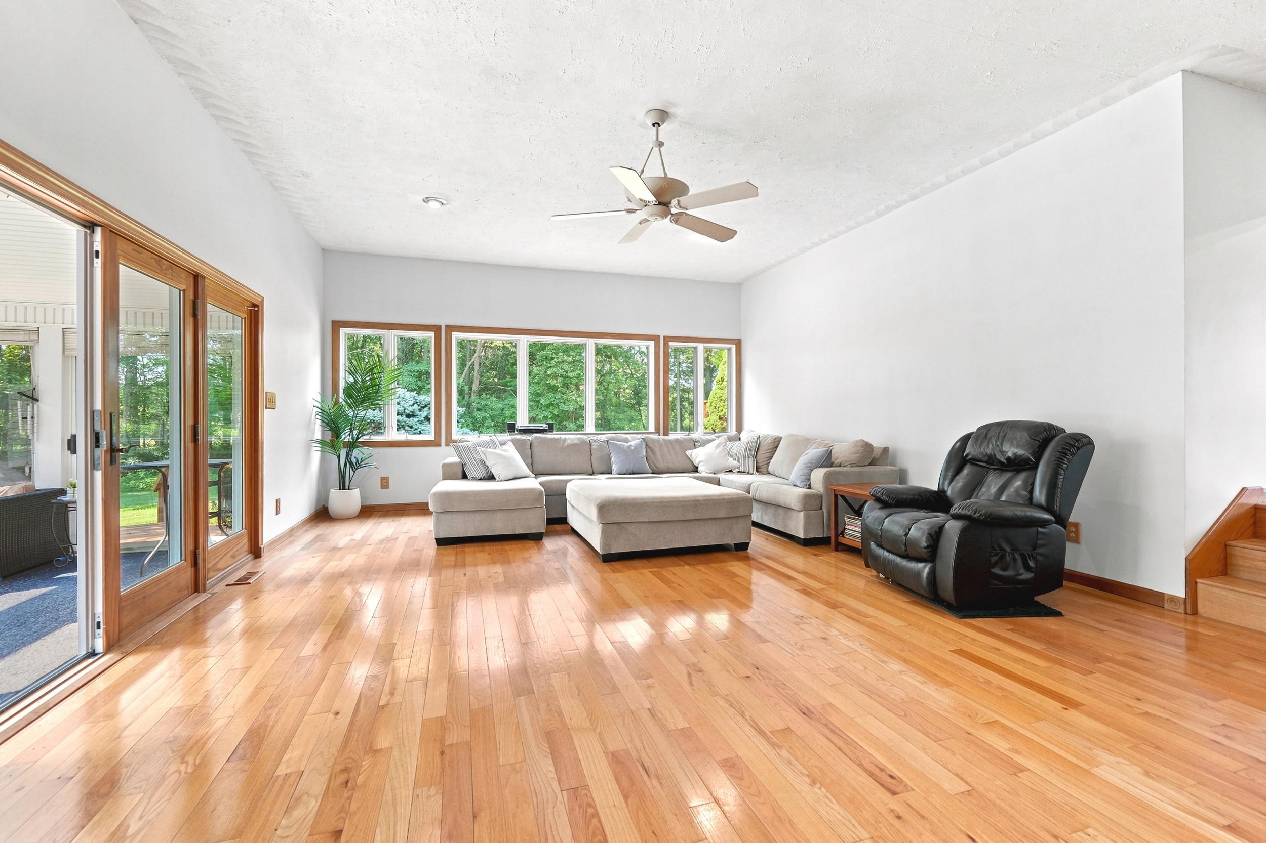 Spacious interior featuring wood-finish flooring, a ceiling fan, and multiple windows with wood trim