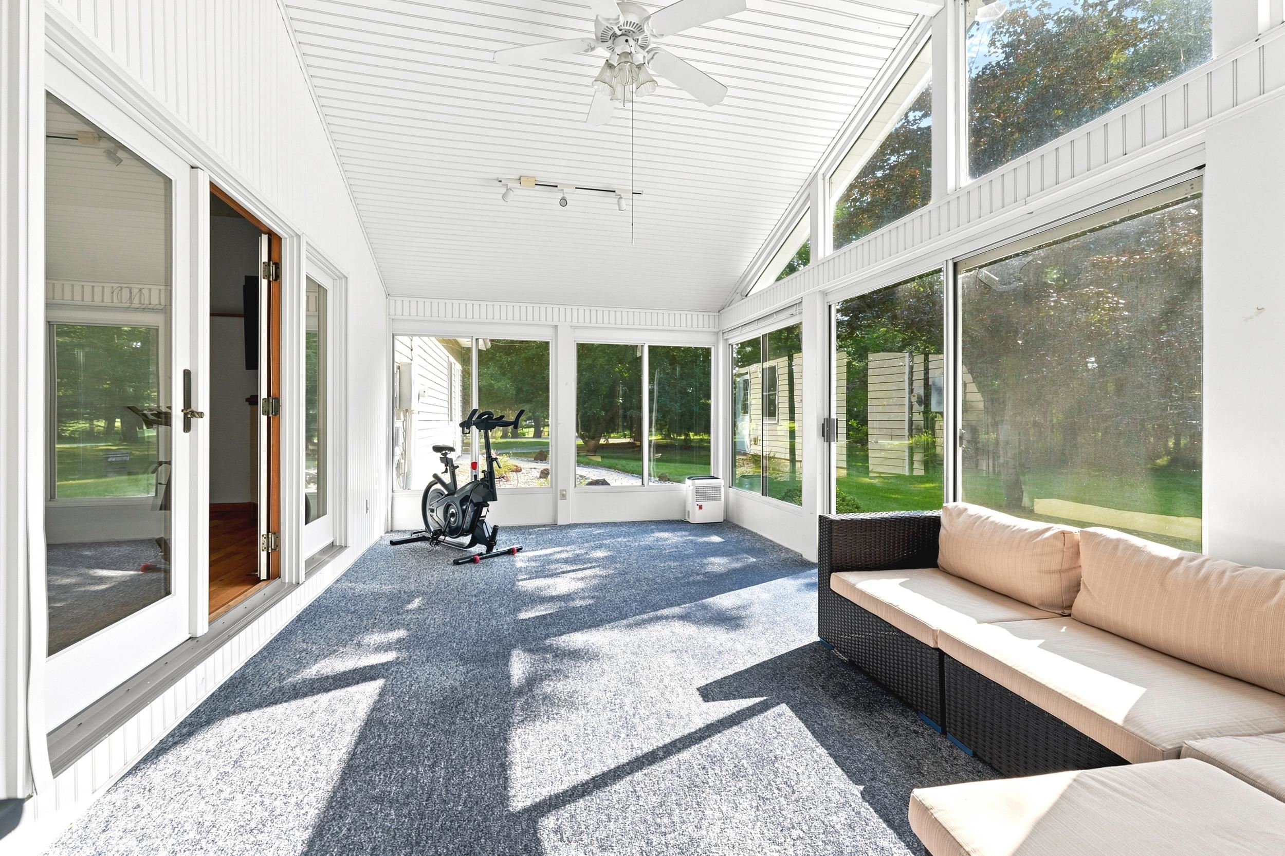 Sunroom featuring extensive fenestration, vaulted ceiling with a ceiling fan, light-toned carpeting, and double glass-paneled doors
