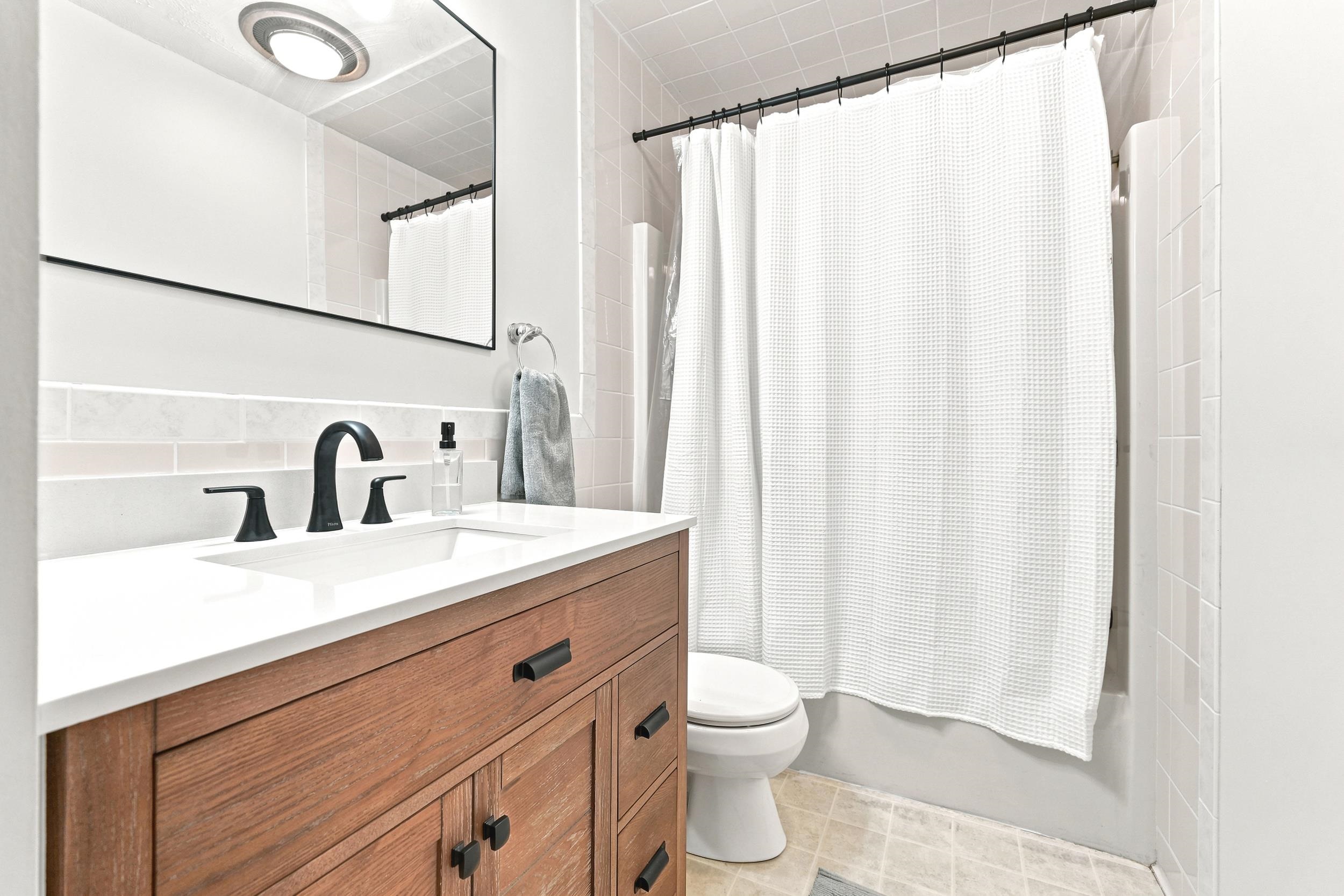 Bathroom featuring a wood-finish vanity with a white countertop, undermount sink, and matte black faucet