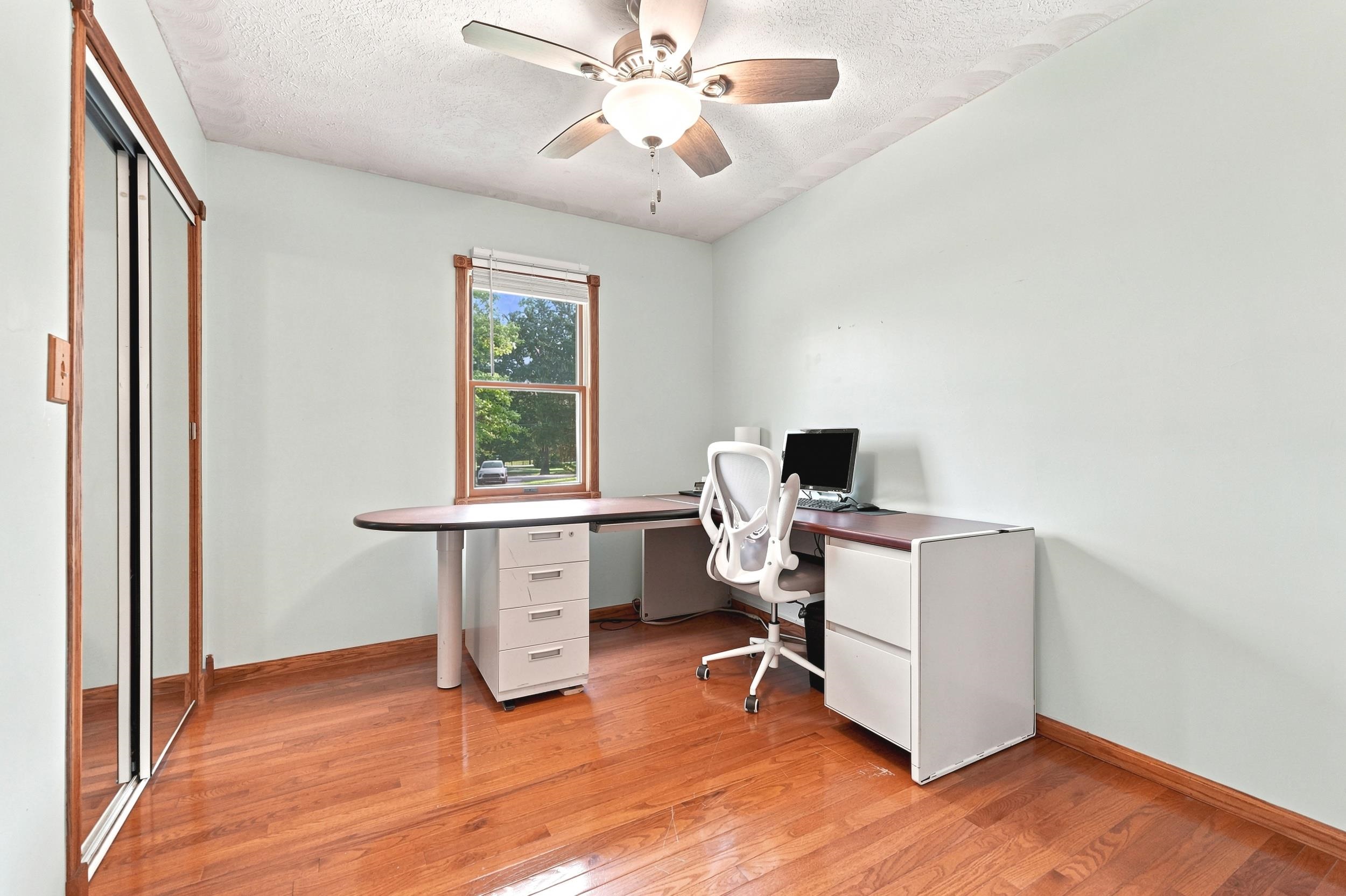 Hardwood flooring throughout featuring a window with natural light, a ceiling fan with integrated lighting, and a closet with bifold mirrored doors