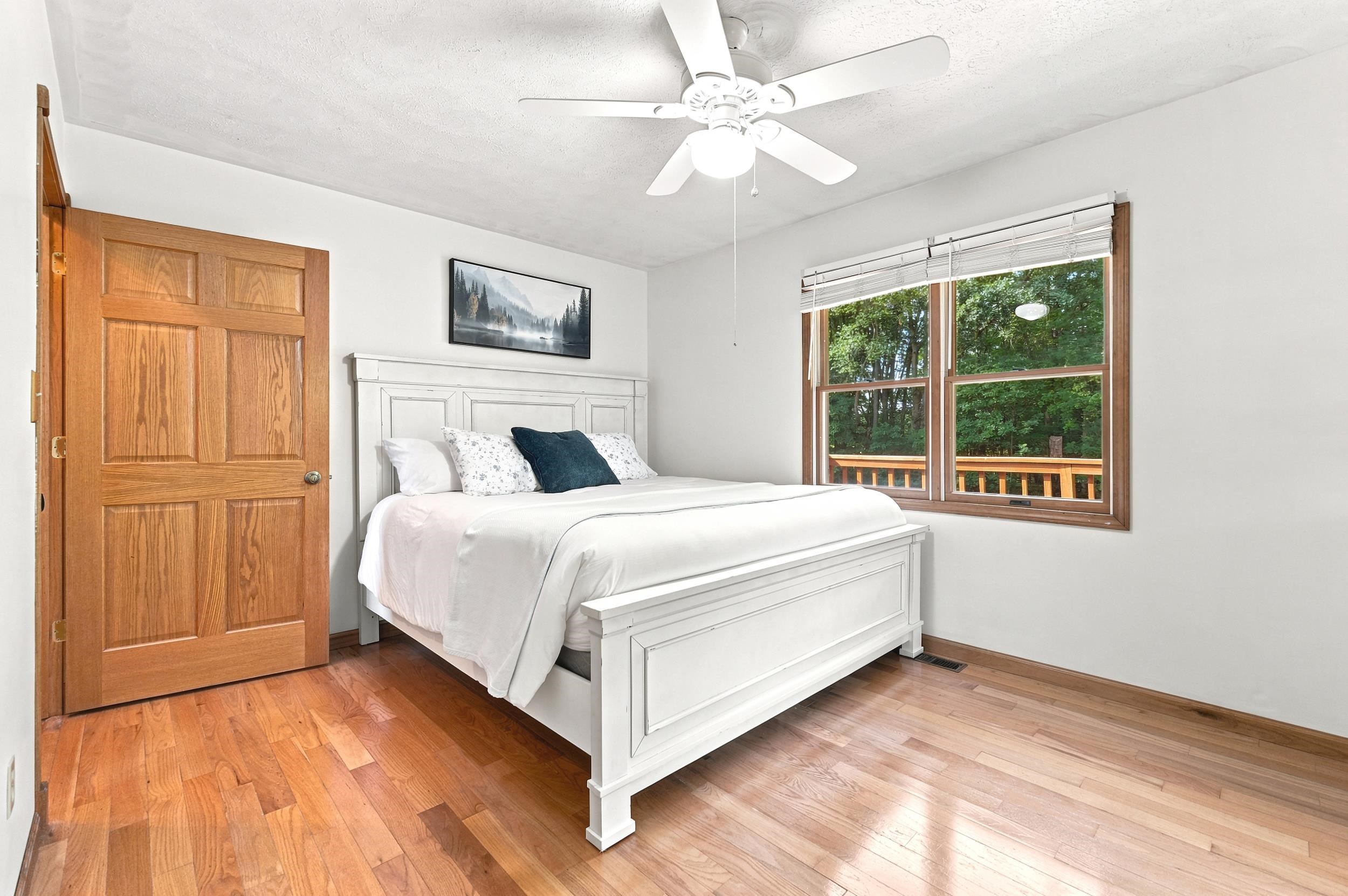 Bedroom featuring wood-finish flooring, a six-panel wood door, and a ceiling fan with light fixture