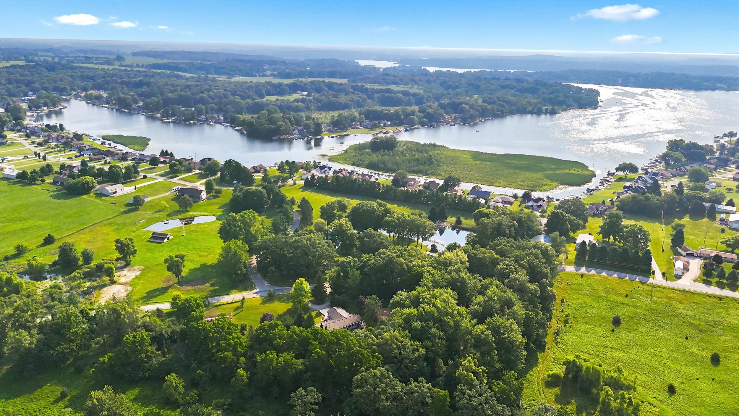 Expansive property featuring a tranquil pond surrounded by mature trees, large green spaces, and a winding road