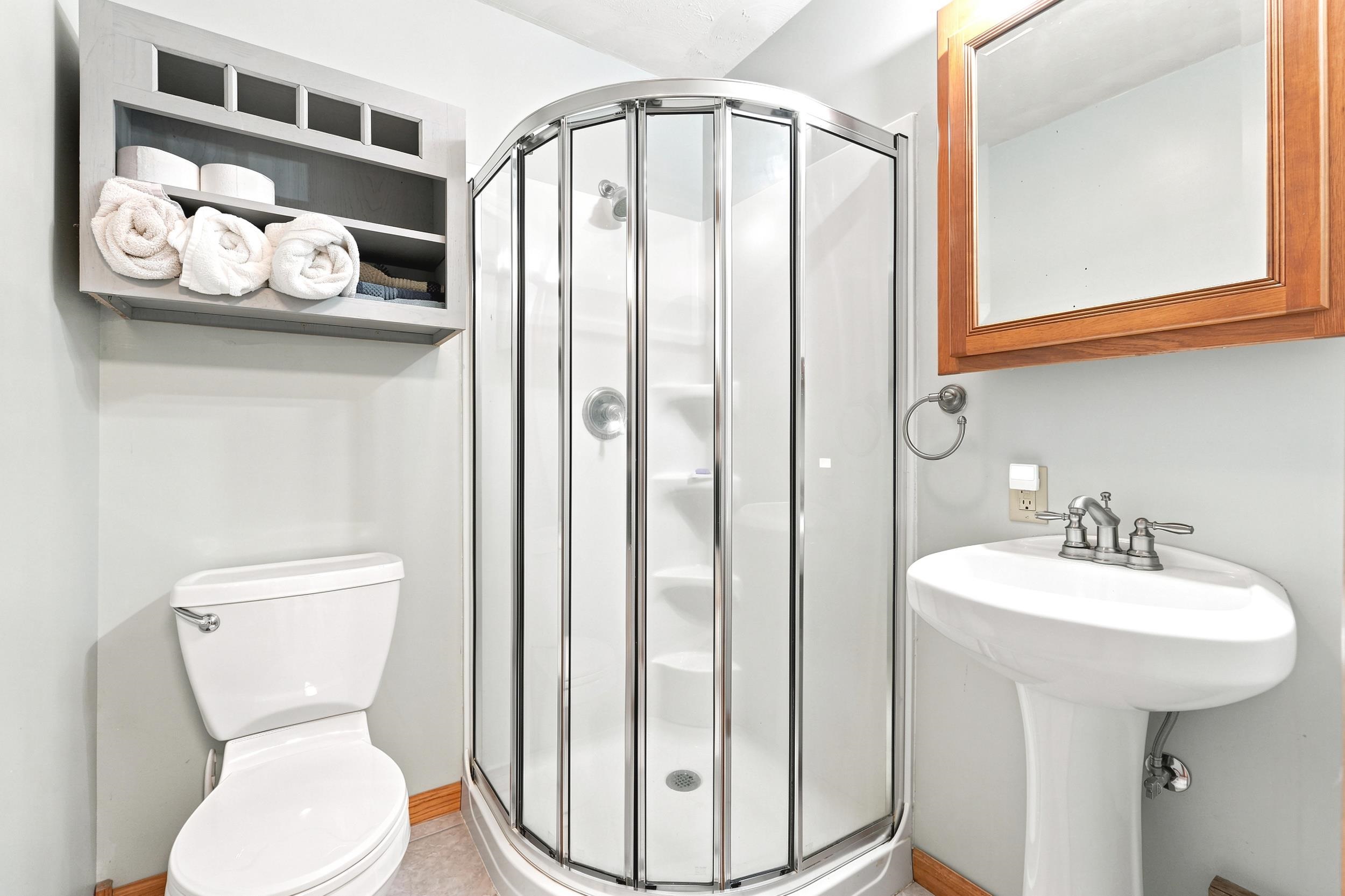 Compact bathroom featuring a corner shower enclosure with clear glass panels, a white pedestal sink with a chrome faucet, and a toilet