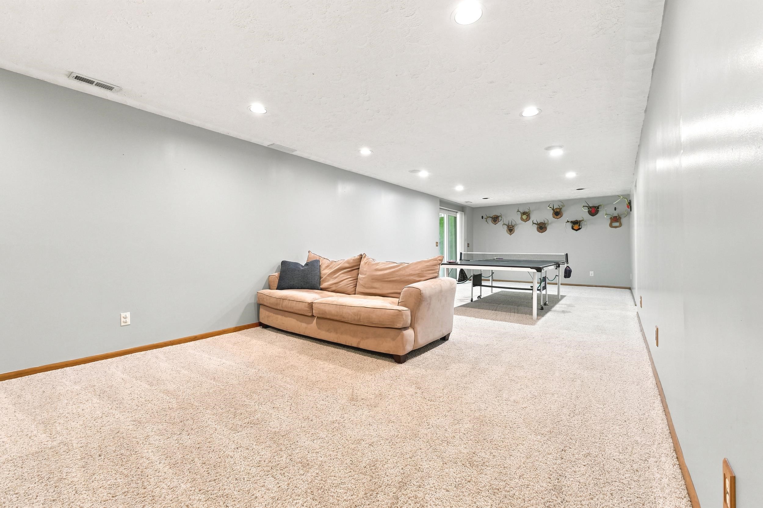 Spacious lower-level room featuring recessed lighting, light-toned carpeting, wood trim, and painted walls