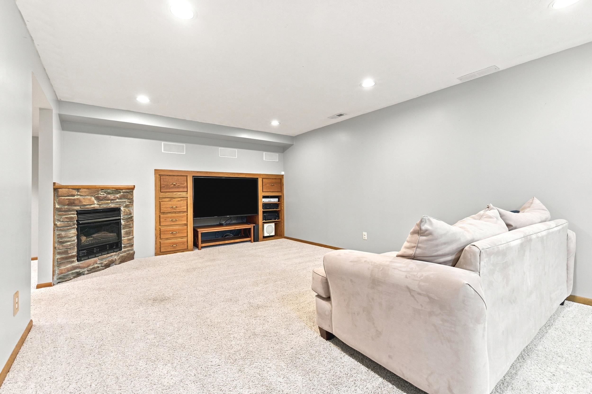 Carpeted room featuring a stone-clad fireplace with a black insert, built-in wood cabinetry, integrated media center, and recessed ceiling lighting