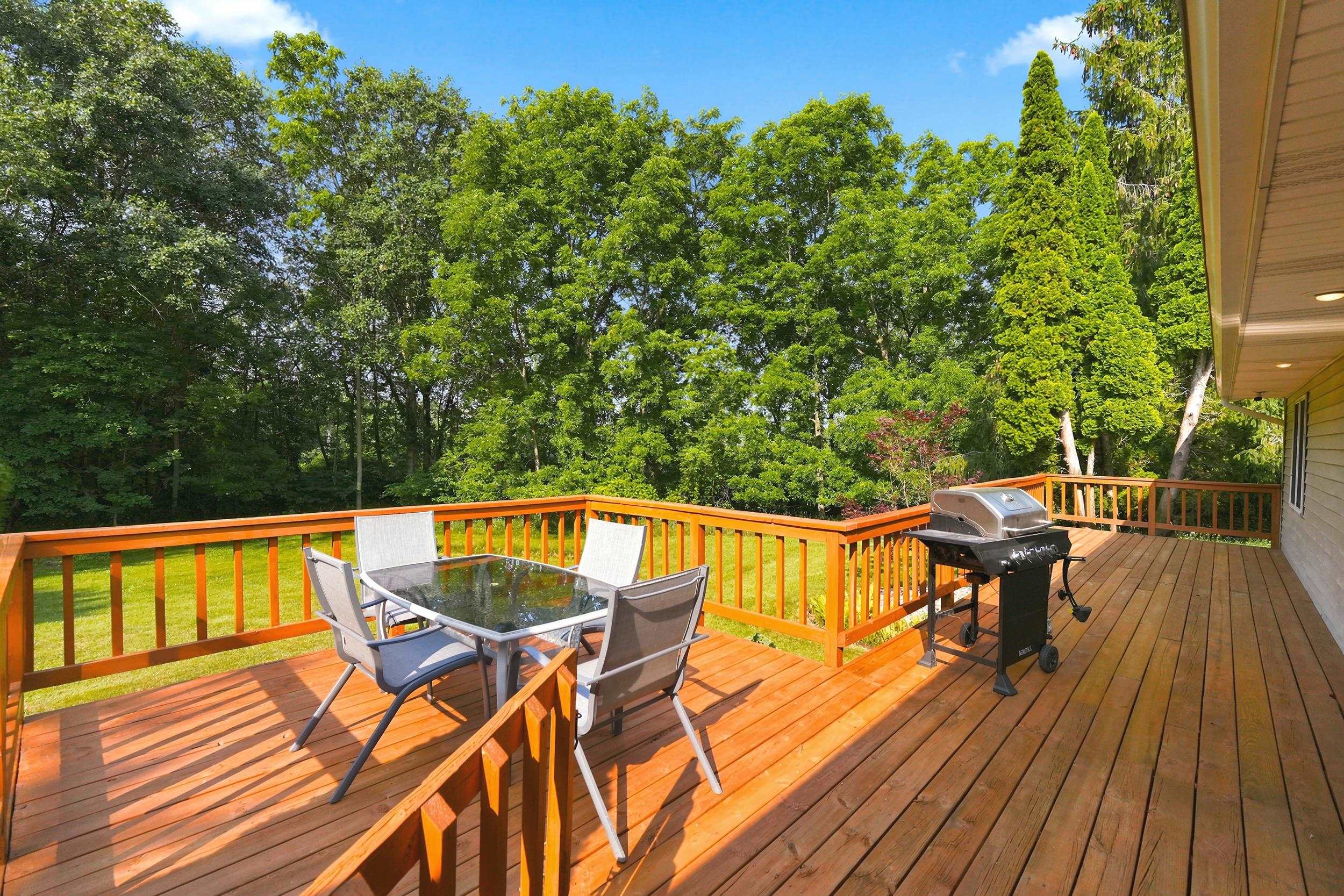 Expansive wood deck with natural wood railing overlooking a grassy yard and mature trees