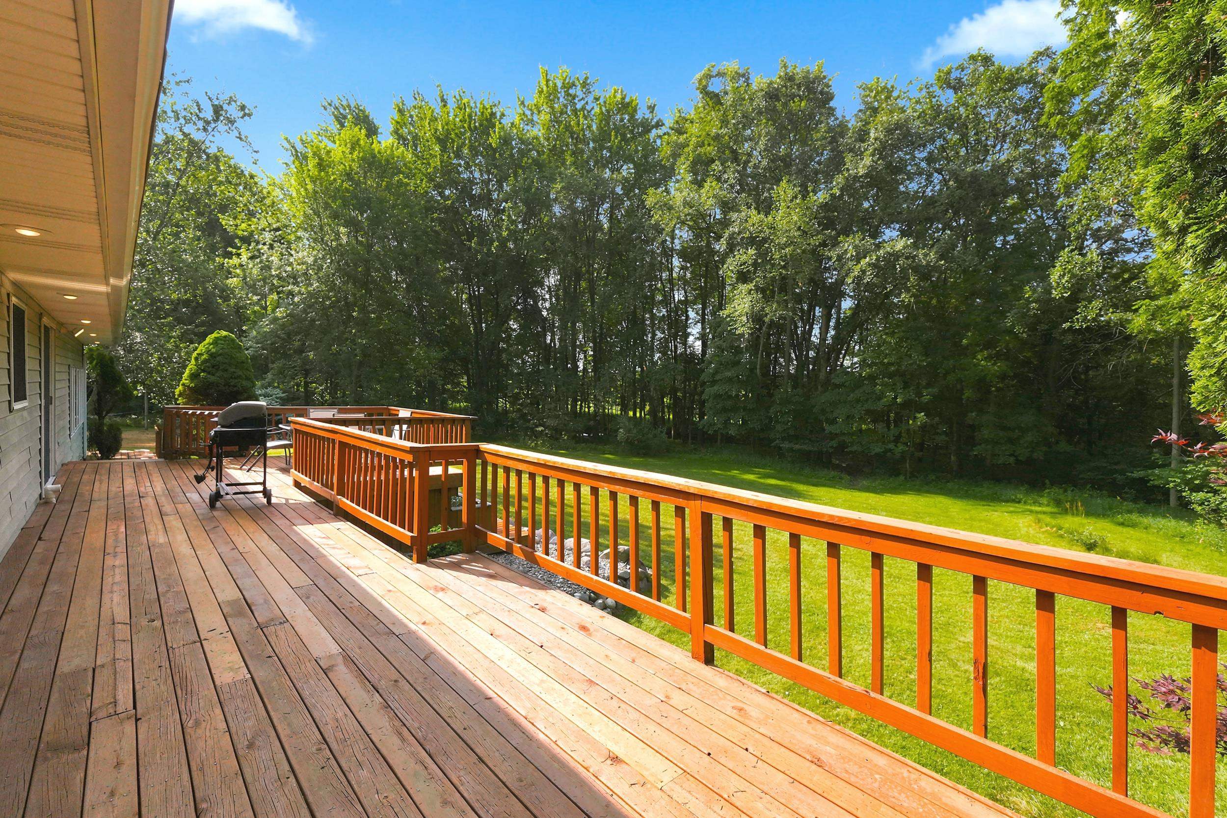 Expansive wood deck with natural wood railings, recessed soffit lighting, and direct access to a grassy yard bordered by mature trees