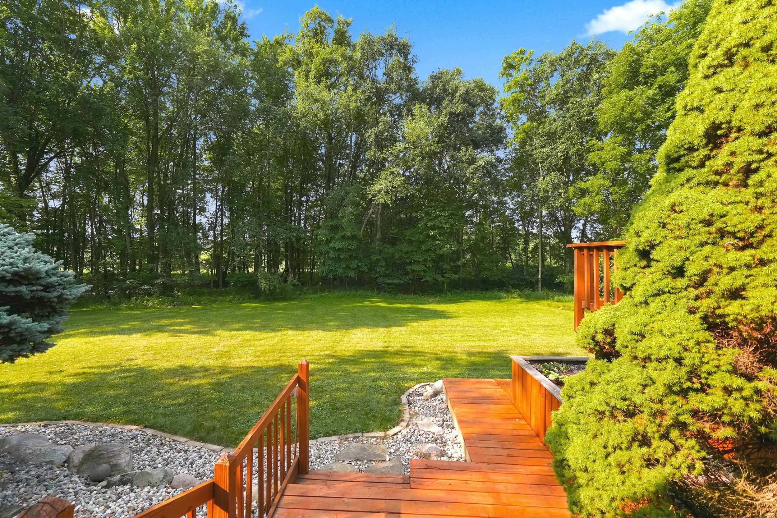 Expansive rear yard featuring a manicured lawn, established landscaping, and mature trees creating a natural border