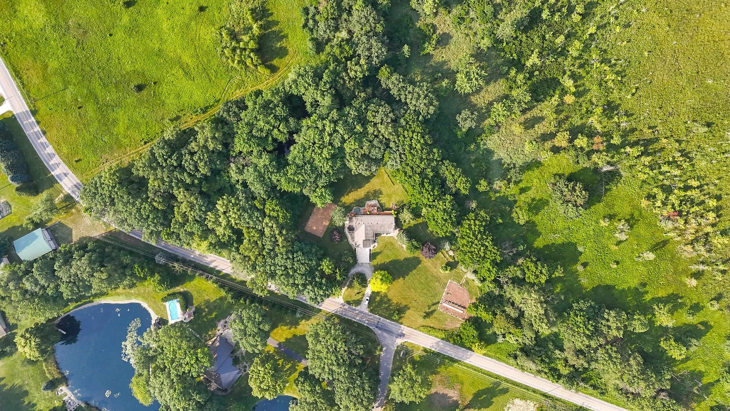 Property featuring a primary residence, extensive tree coverage, and surrounding open green space