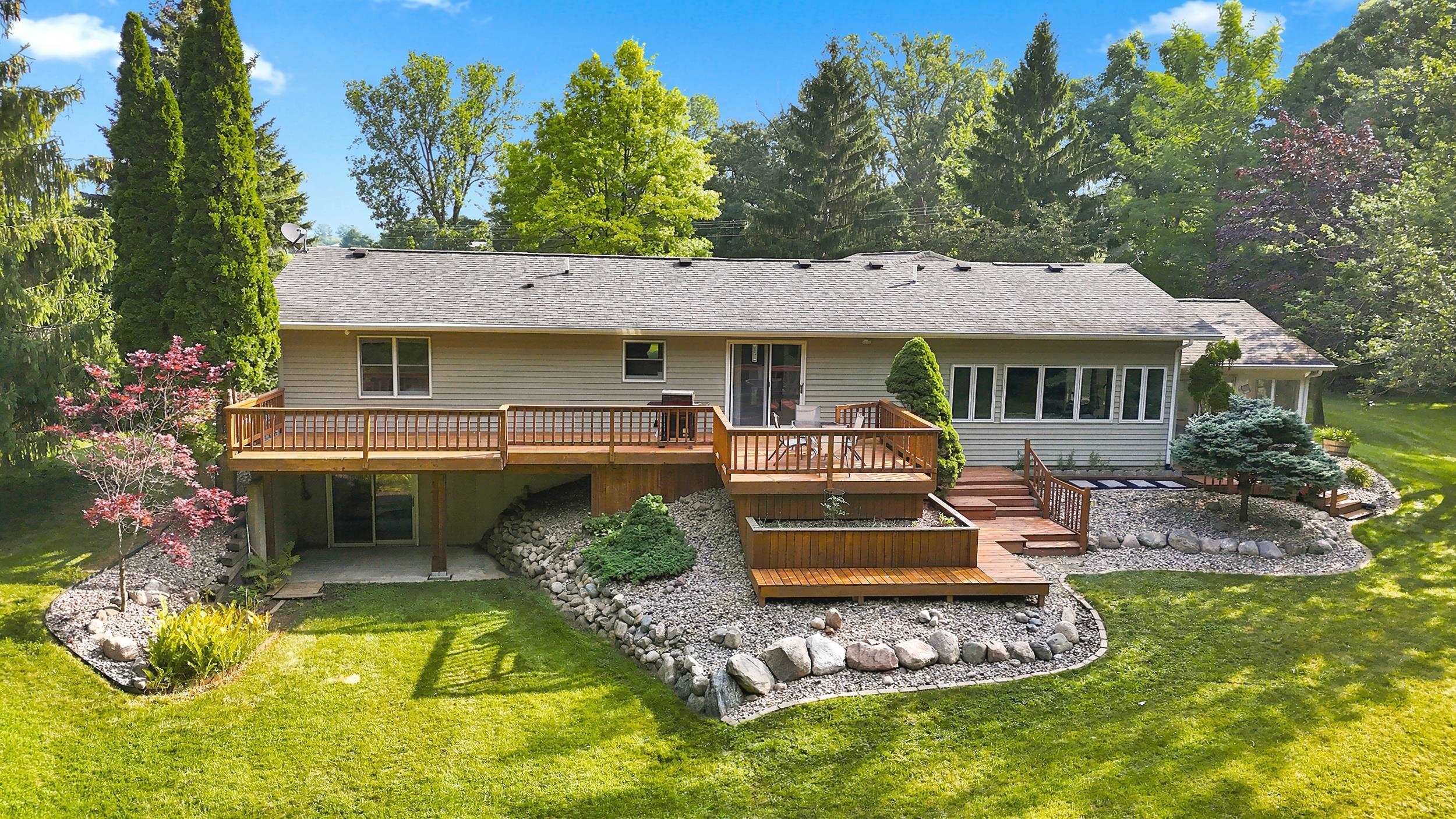 Multi-level wood deck overlooking a spacious green lawn, surrounded by mature trees and natural landscaping