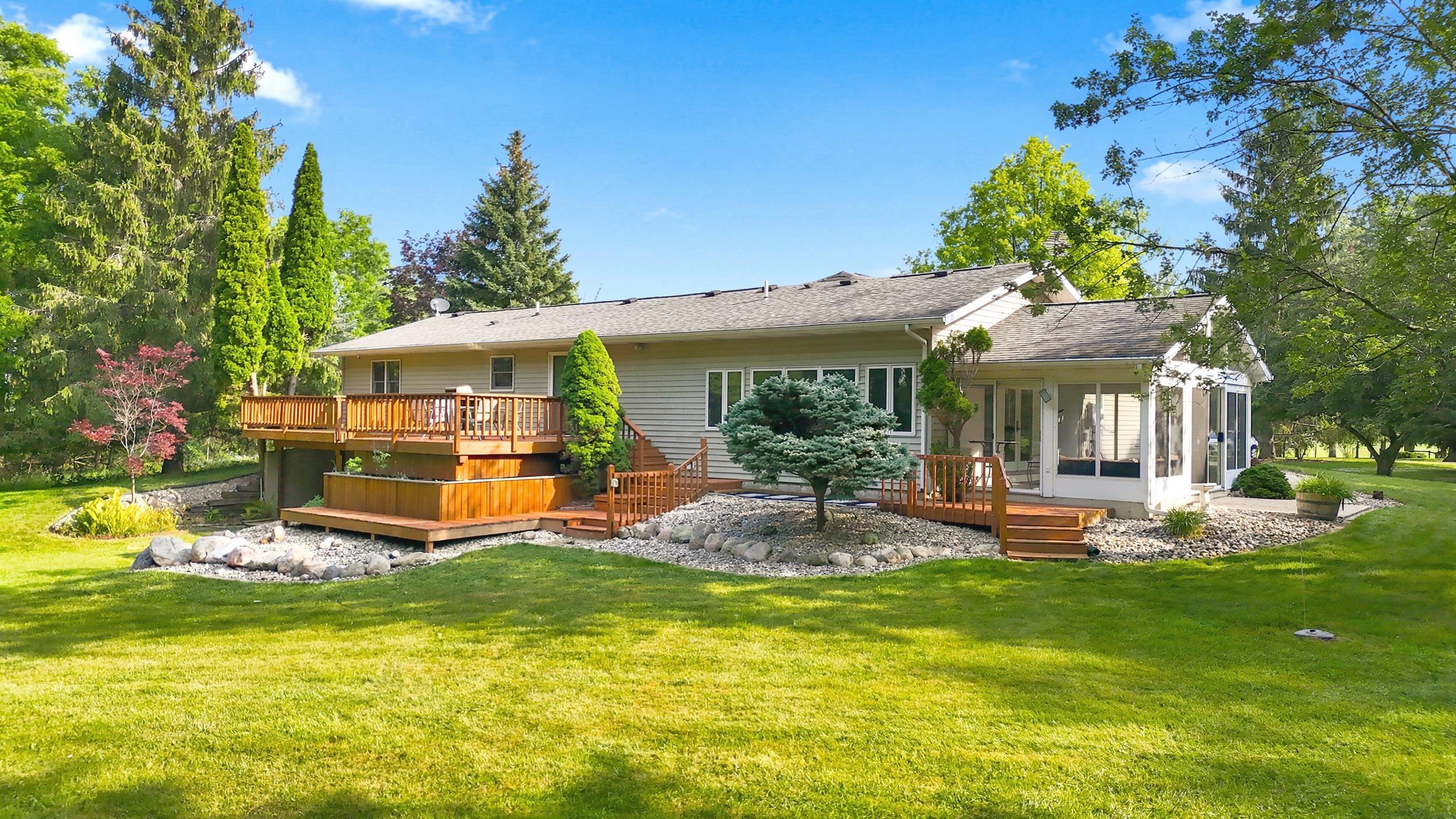 Rear exterior featuring a multi-level wood deck, an enclosed screen porch, and a gravel rock garden