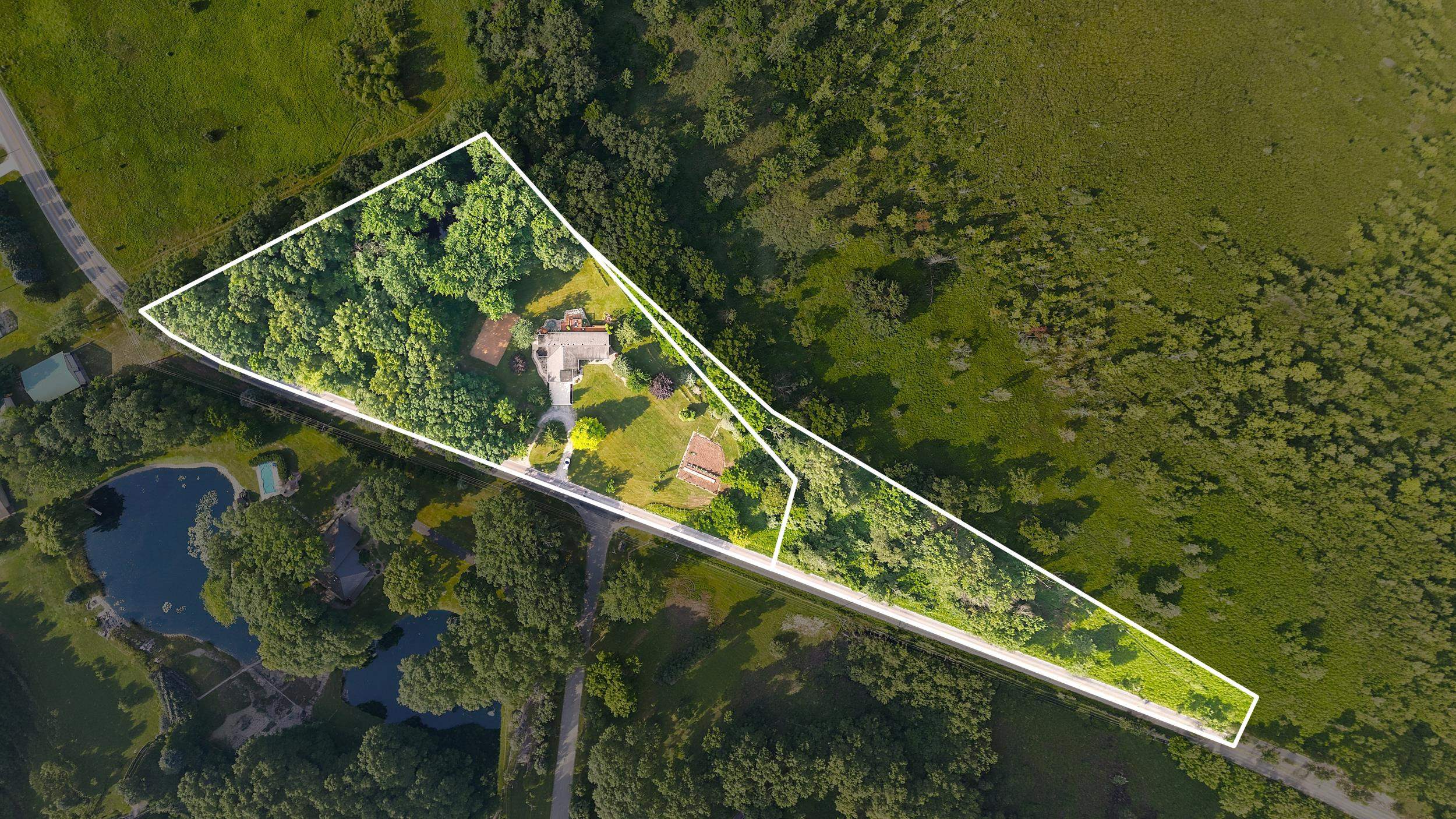Aerial overview showcasing a property boundary with a primary residence, additional structures, and a pond