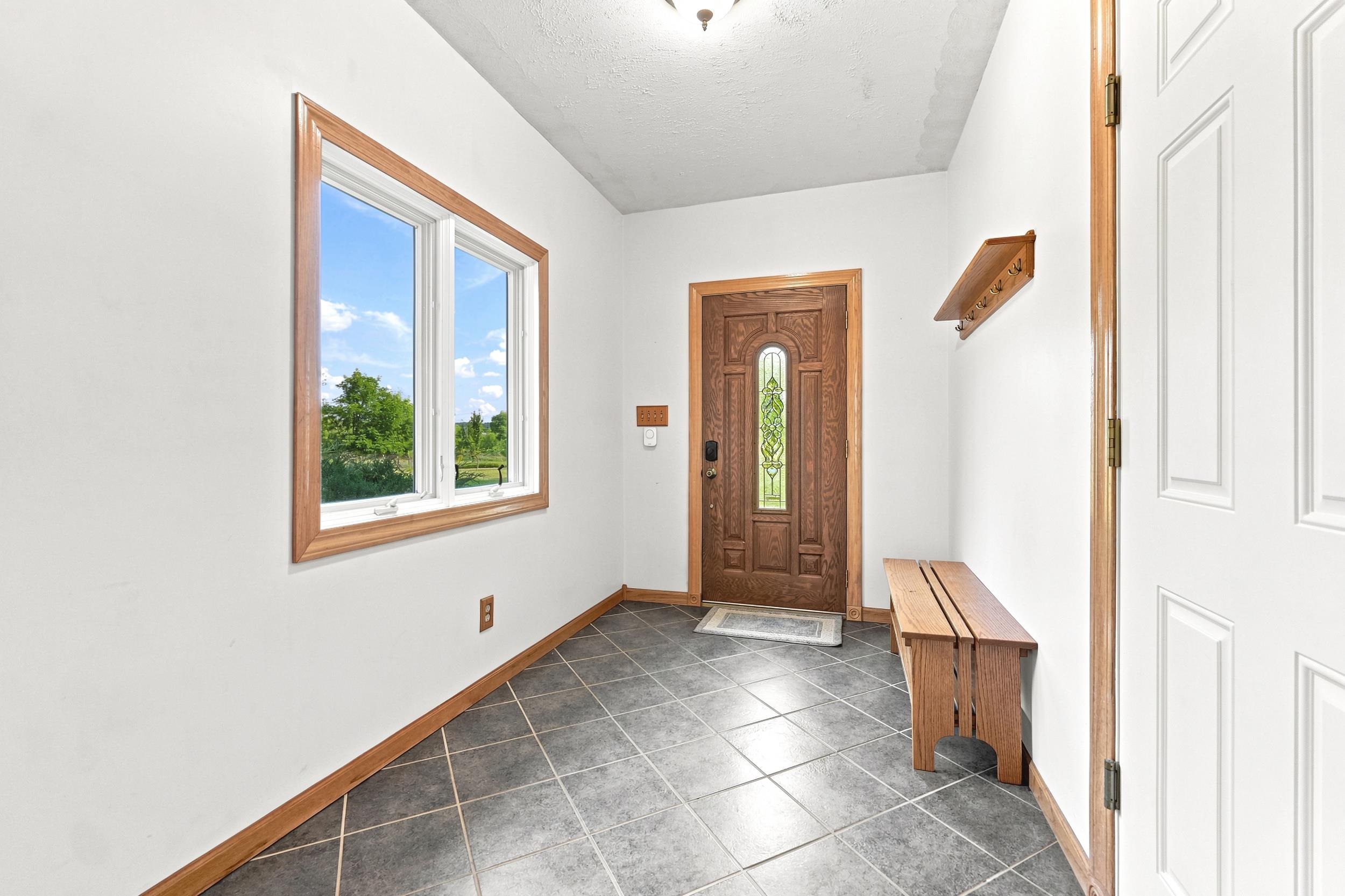 Entryway featuring dark square tile flooring, a large window with wood trim, and a decorative wood entry door with an arched glass insert