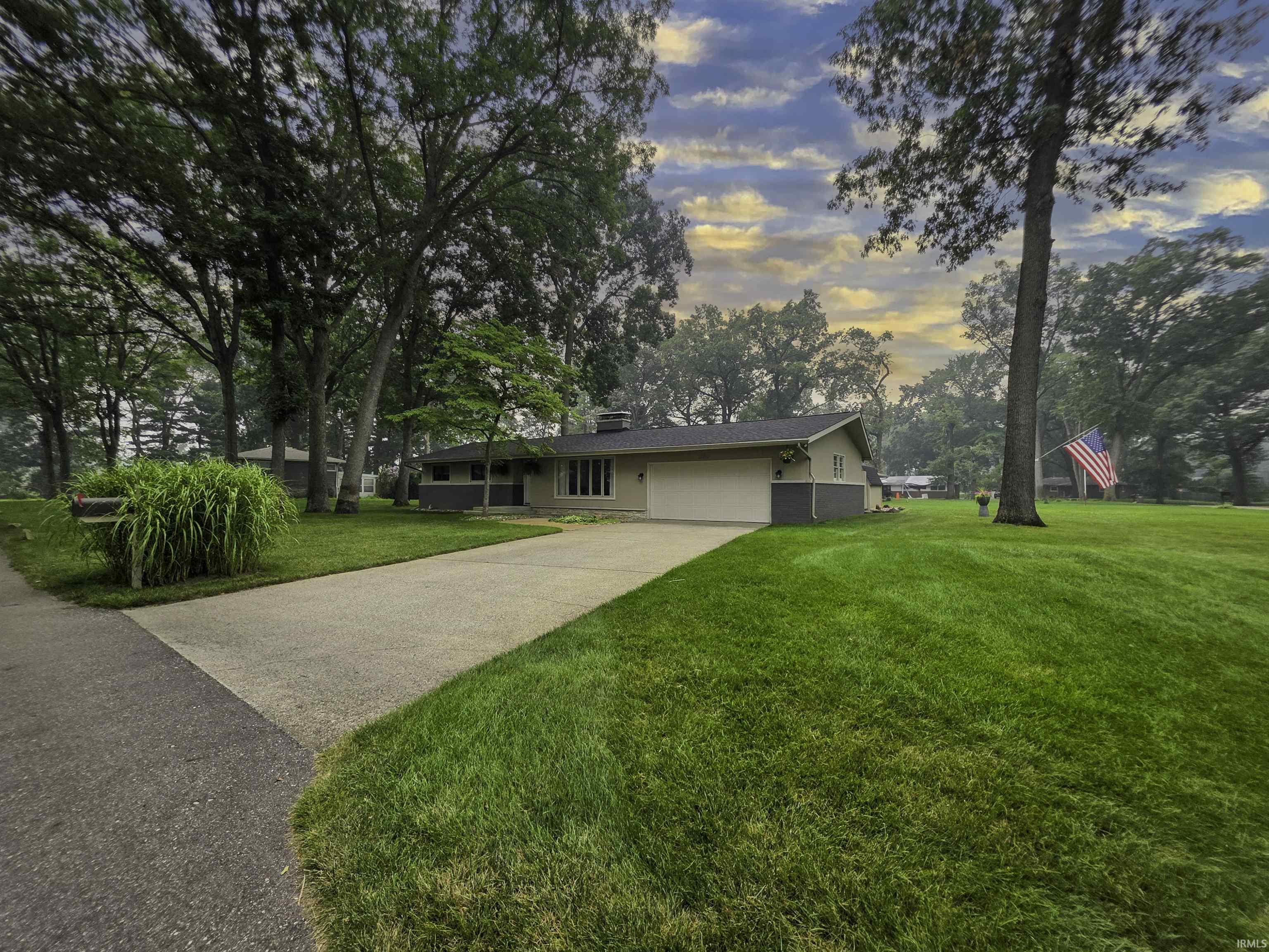Ranch-style residence featuring an attached two-car garage, concrete driveway, and a stone chimney