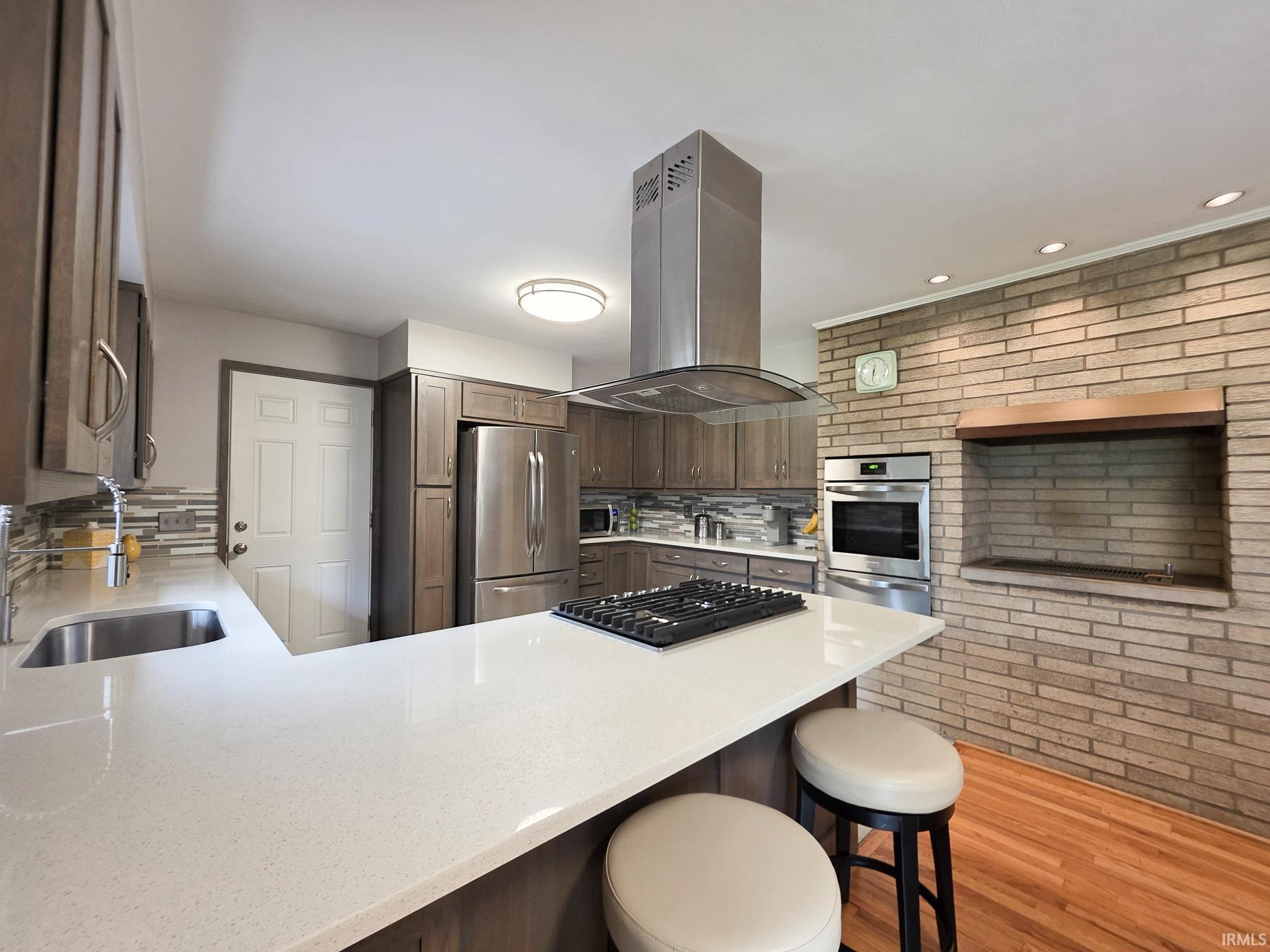 Modern kitchen featuring a U-shaped white countertop, stainless steel appliances, a built-in cooktop, and a brick accent wall with a recessed area