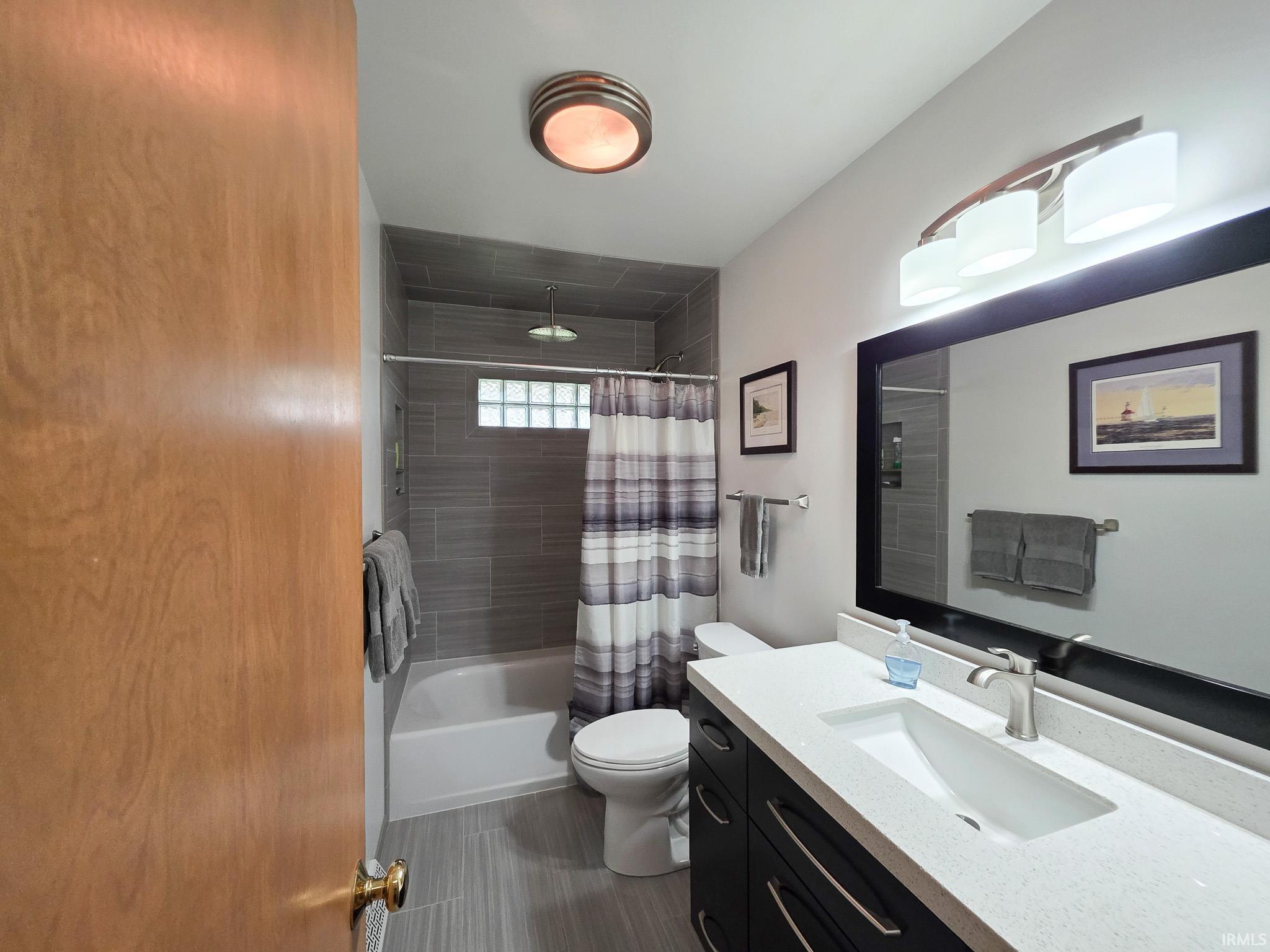 Renovated full bathroom with tile shower and rain shower head, large vanity with a lot of storage space.