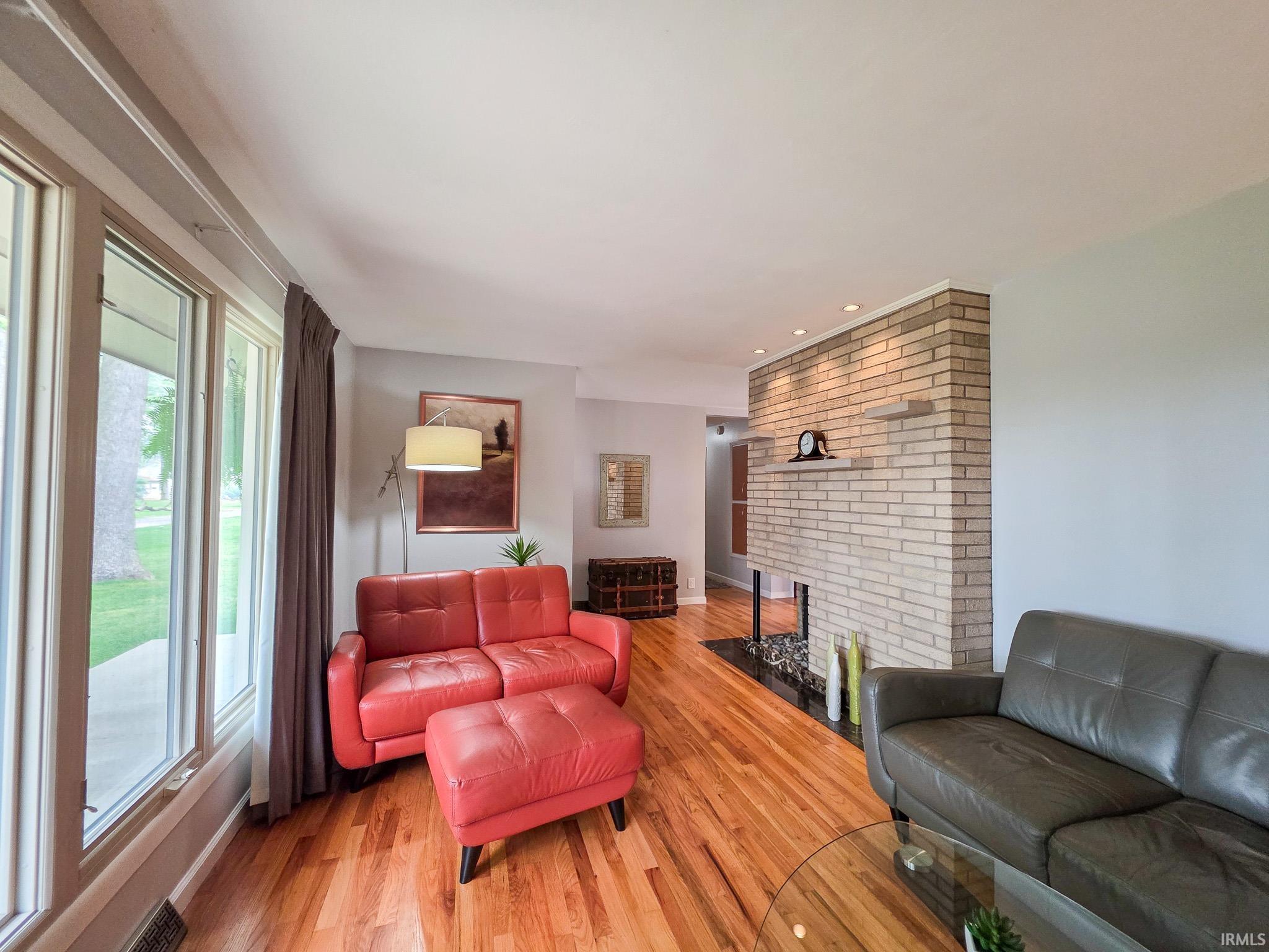 Living area featuring wood-finish flooring, a light brick fireplace with a black hearth, and recessed lighting