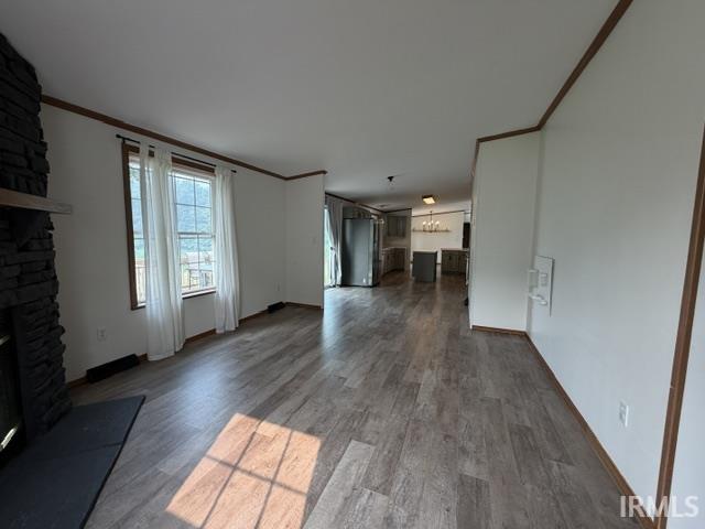 Open-concept living space featuring wood-finish flooring, a stone-clad fireplace with a wood mantle, and bright white walls with dark trim