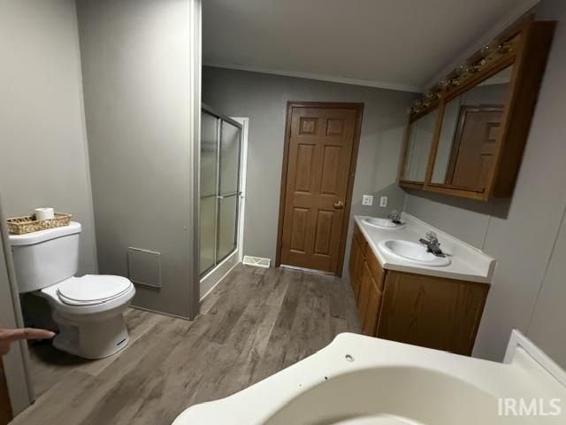 Bathroom featuring a double vanity, wood-finish flooring, and a shower with glass enclosure