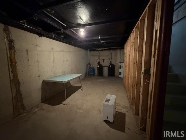Unfinished basement space featuring exposed concrete walls and flooring, overhead utility lines, and framed wall sections