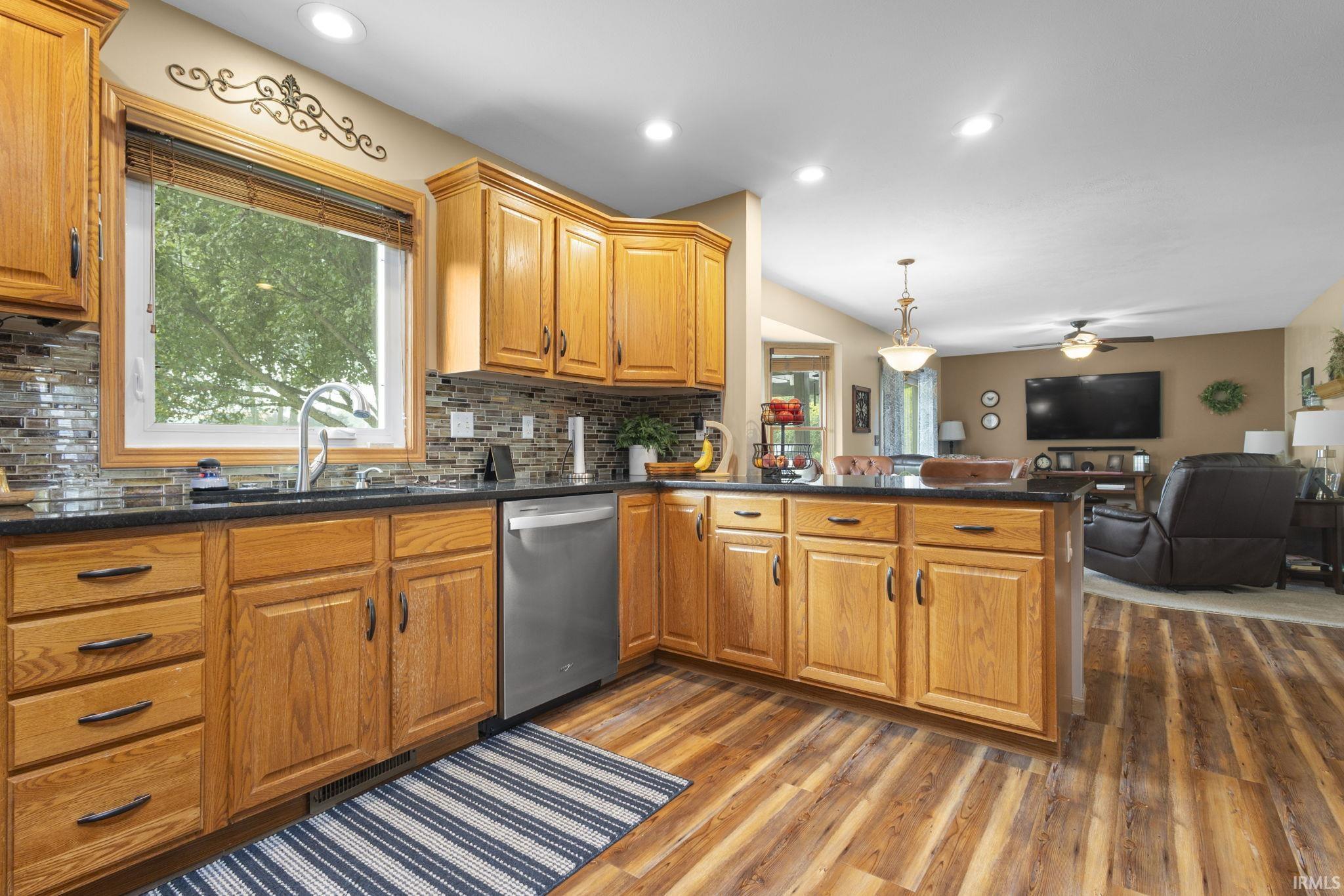 Kitchen featuring wood cabinetry, dark countertops, a mosaic tile backsplash, and a stainless steel dishwasher
