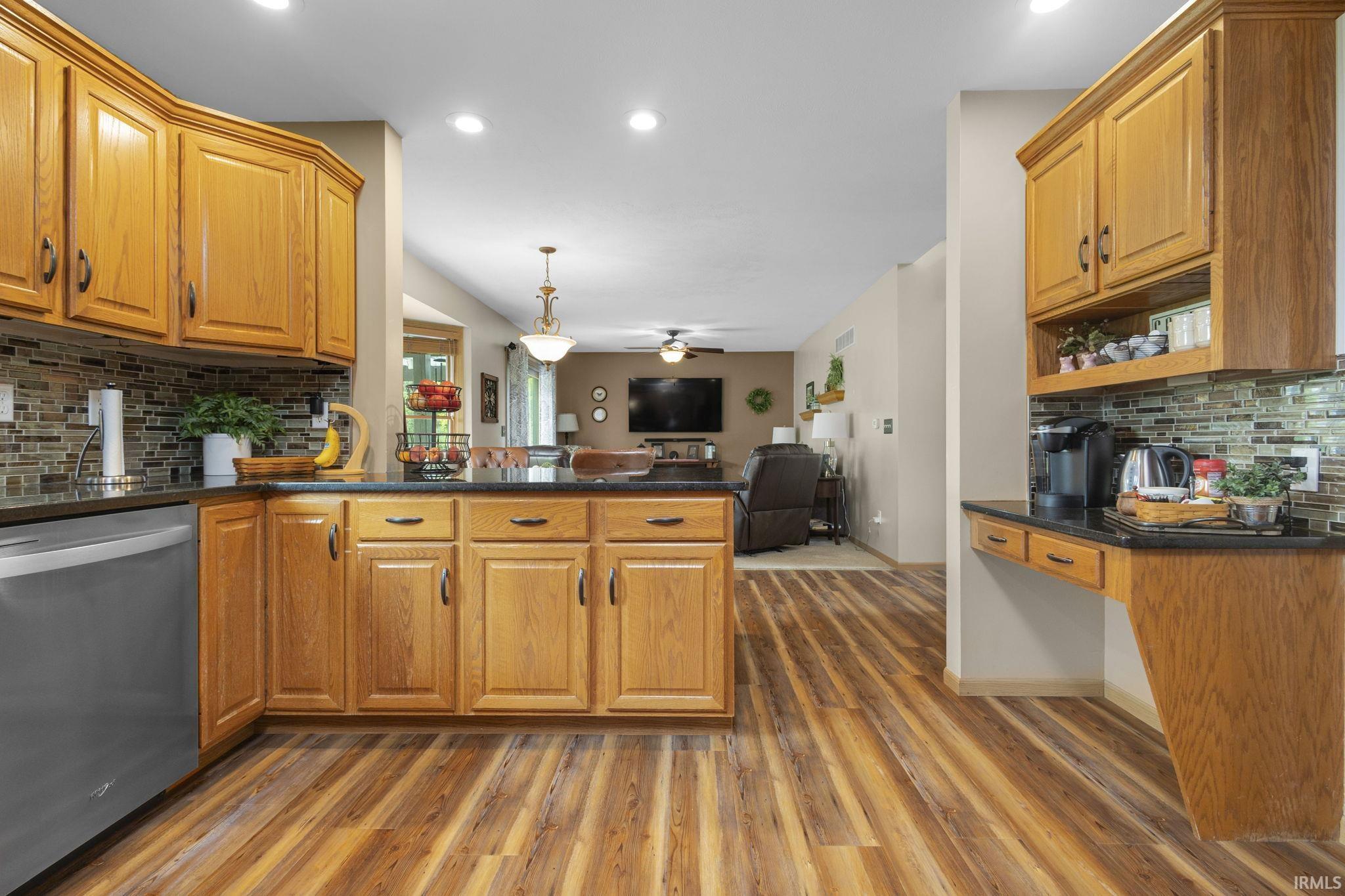 Kitchen featuring wood-finish flooring, oak cabinetry, dark countertops, and a mosaic tile backsplash