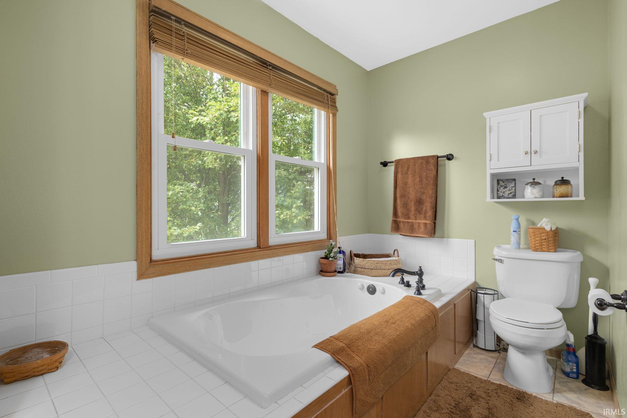 Bathroom featuring a built-in soaking tub with dark-finished fixtures, white ceramic tile surround, and a wood-finish tub deck
