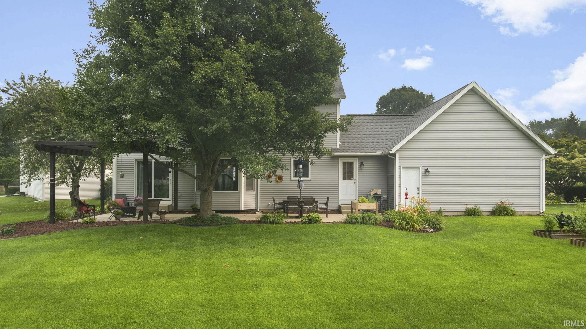 Expansive backyard featuring a large concrete patio, a pergola structure, and a mature shade tree