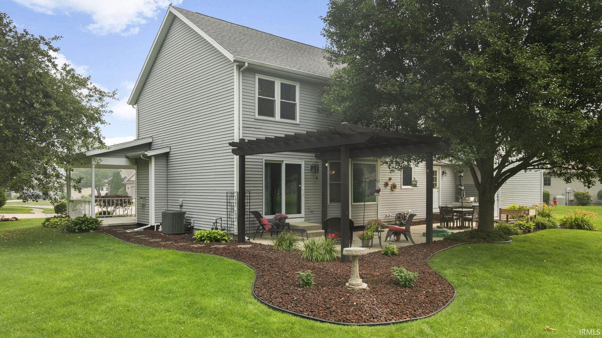 Rear exterior featuring gray siding, a screened porch, a patio with a dark wood pergola, a mature tree, and landscaped beds with dark mulch