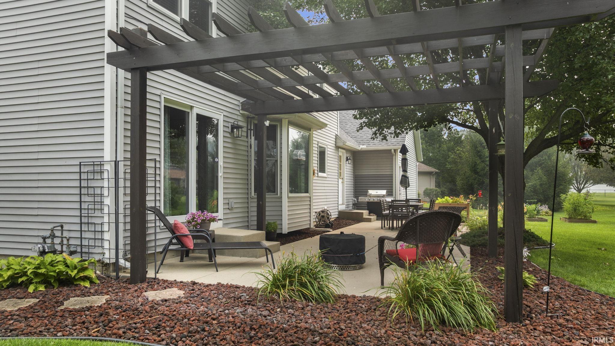 Expansive concrete patio with a dark-stained pergola, surrounded by red decorative rock and landscaping