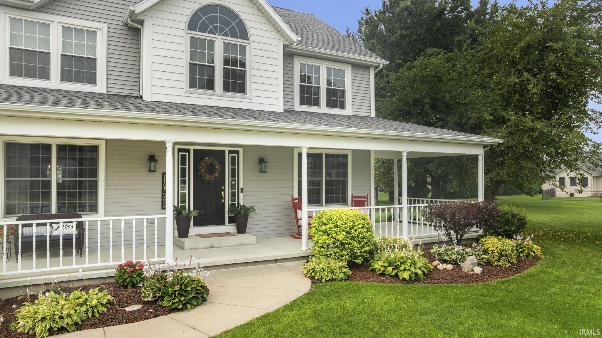 Two-story residential exterior featuring light-colored siding, a full-width covered porch with white railings, and a prominent arched window dormer