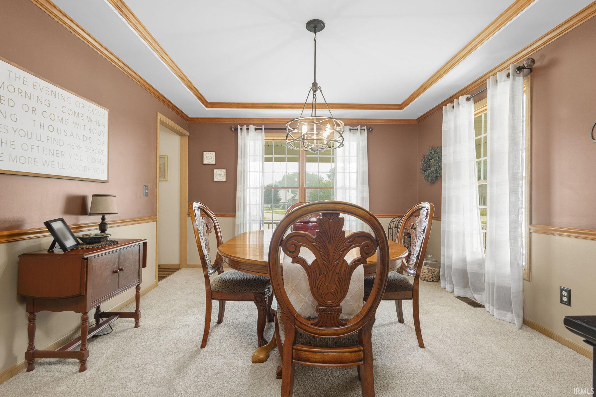 Dining space featuring a tray ceiling with wood trim, neutral carpet flooring, and dual windows