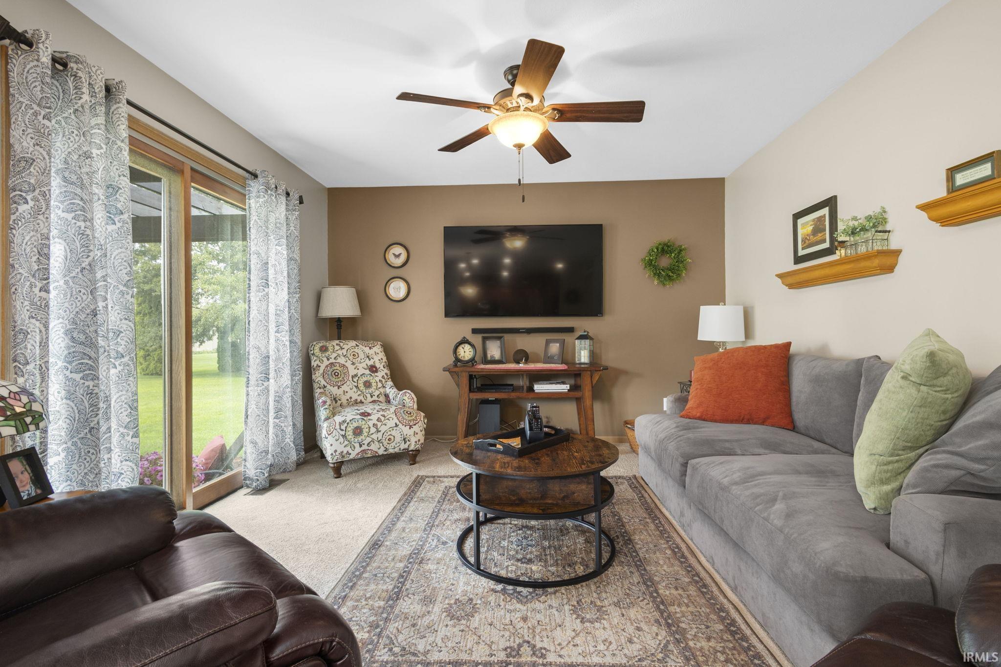 Living area featuring a sliding glass door, neutral-toned carpeting, a ceiling fan with integrated lighting, and a mounted television