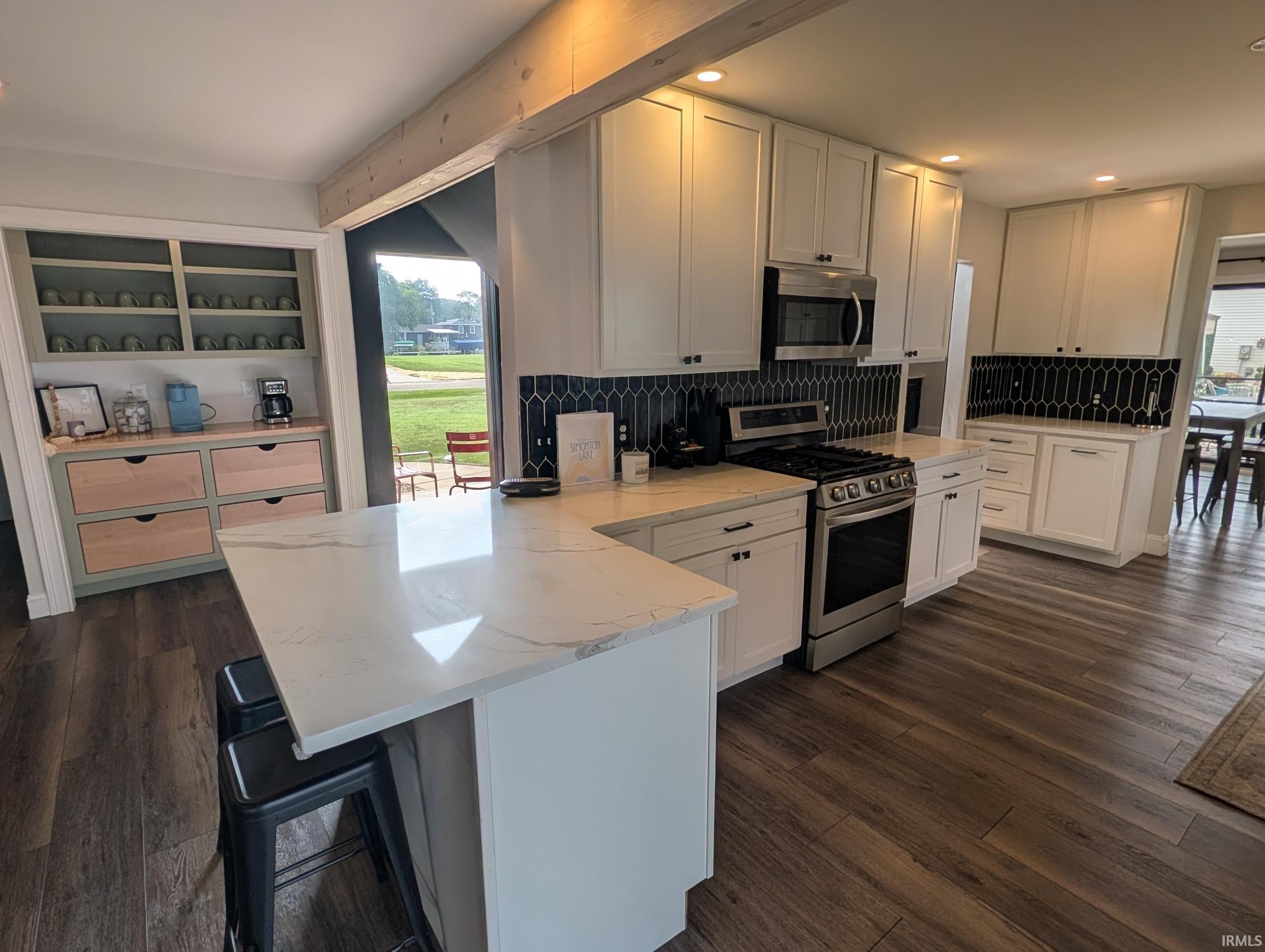 Open-concept kitchen featuring white shaker cabinetry, stainless steel appliances, and a black picket tile backsplash