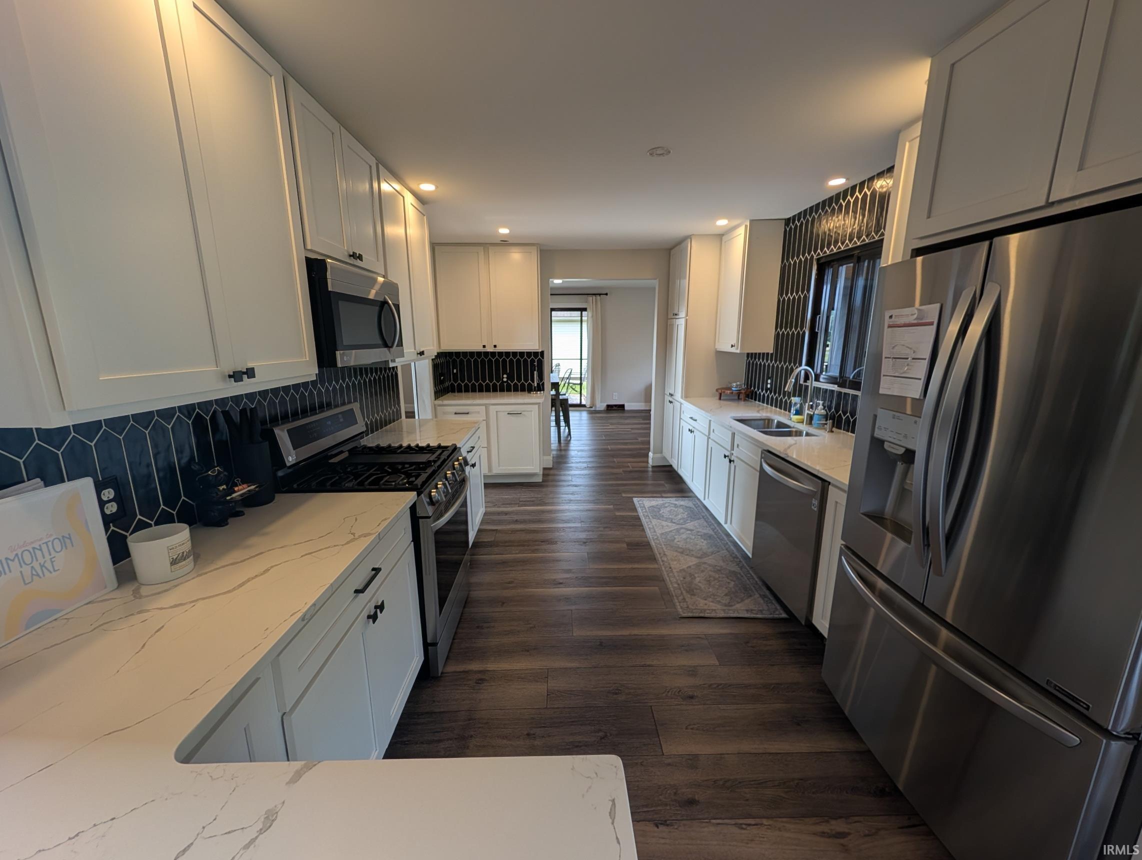 Gourmet kitchen featuring extensive white cabinetry, quartz countertops with subtle veining, wood-finish flooring, a stainless steel appliance suite, and a distinctive dark geometric tile backsplash