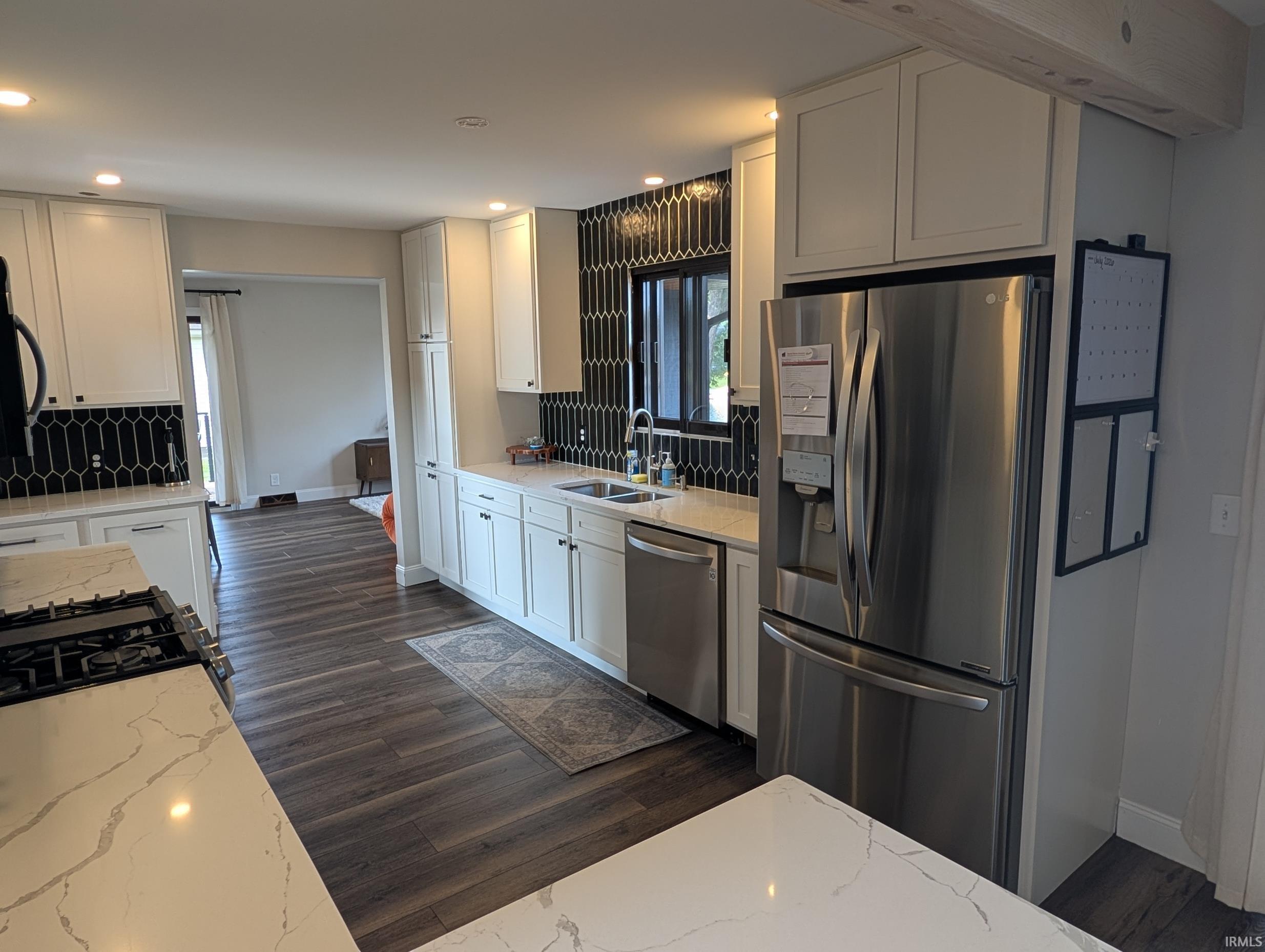 Kitchen featuring white cabinetry, wood-finish flooring, quartz countertops, a black picket tile backsplash, and stainless steel appliances