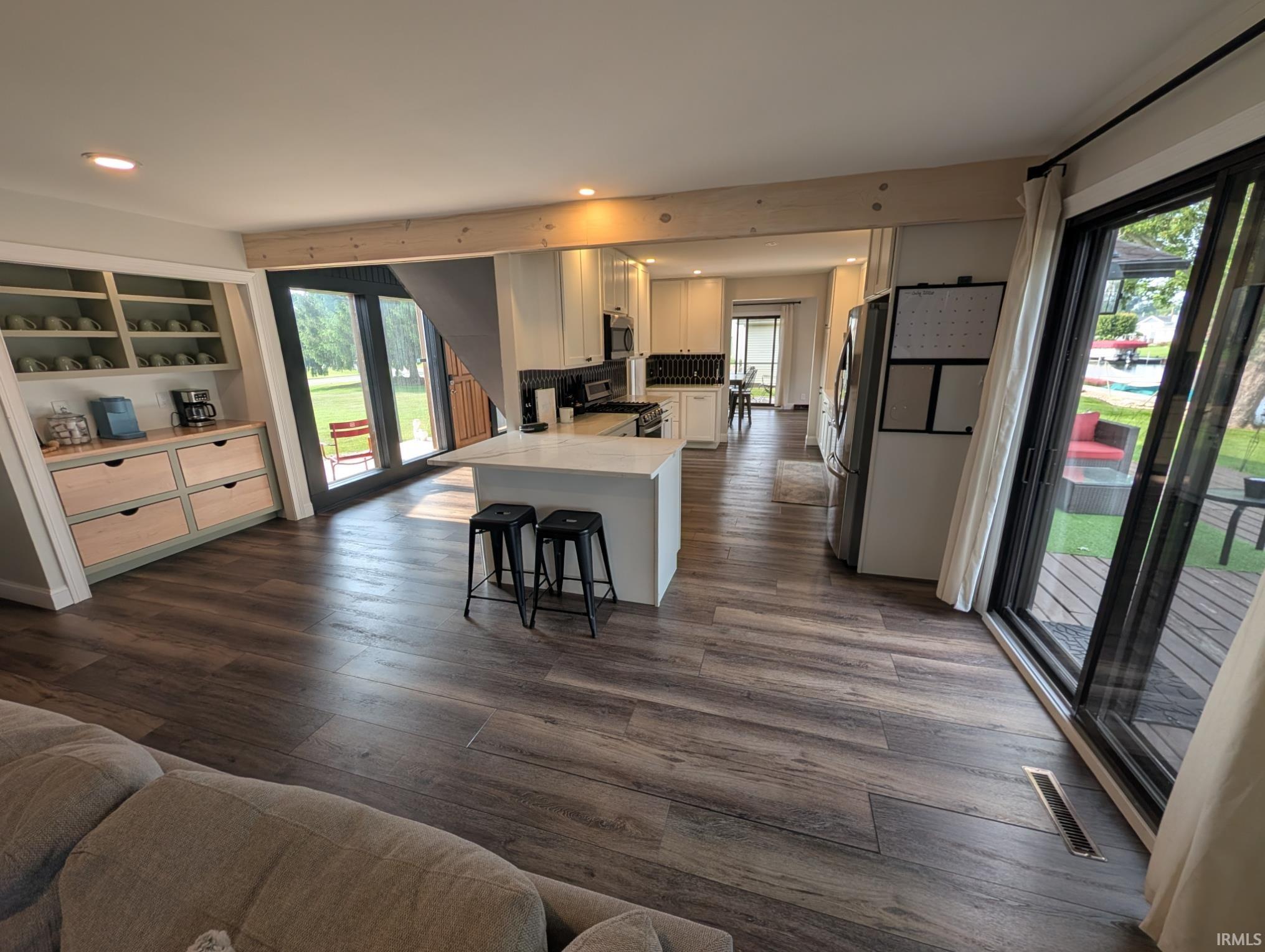 Open-concept living area featuring wood-finish flooring, a central kitchen island with a light-colored countertop, and a built-in shelving unit with drawers