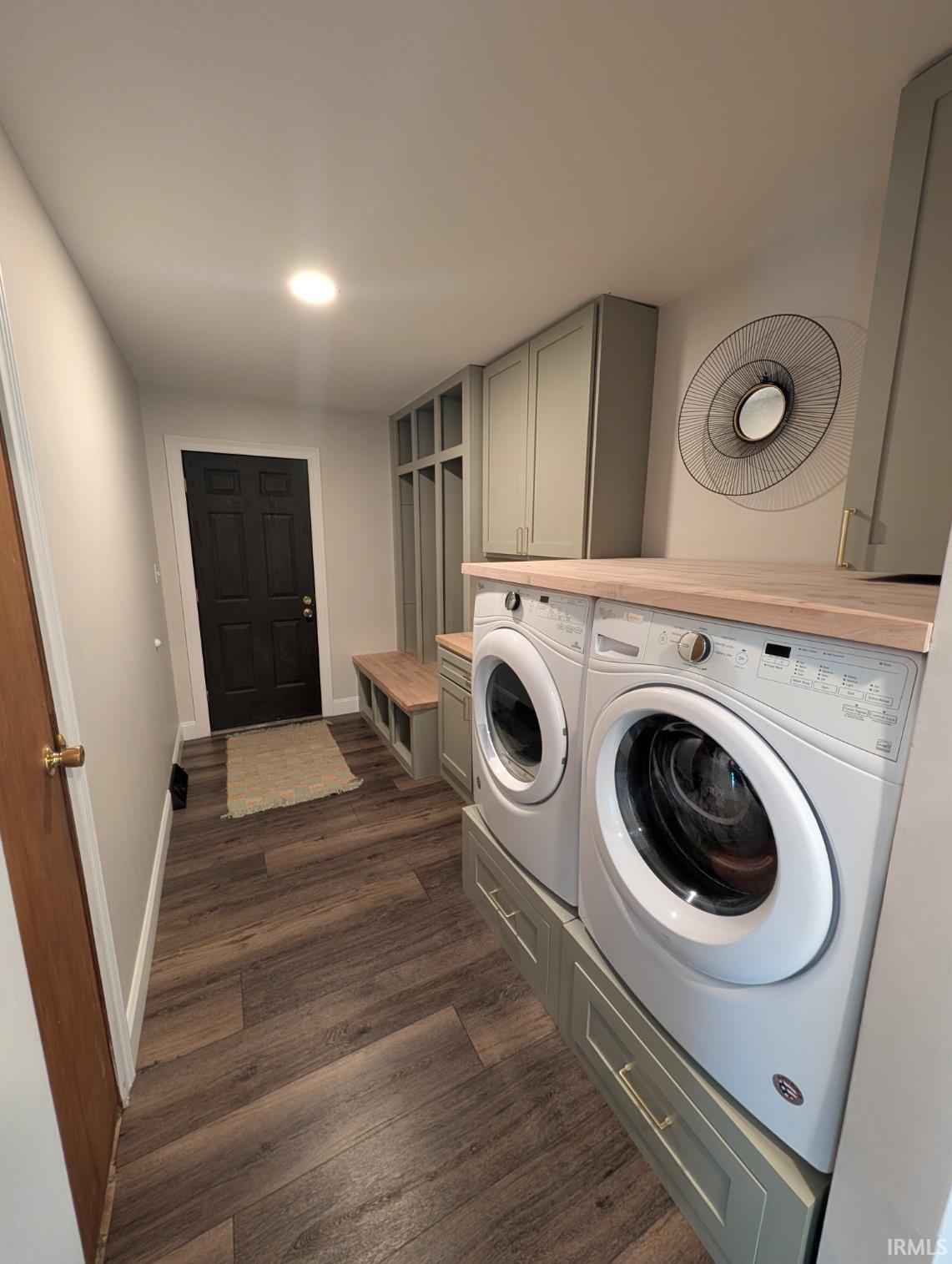 Dedicated laundry area featuring modern front-load appliances with custom cabinetry, wood-finish flooring, and recessed lighting