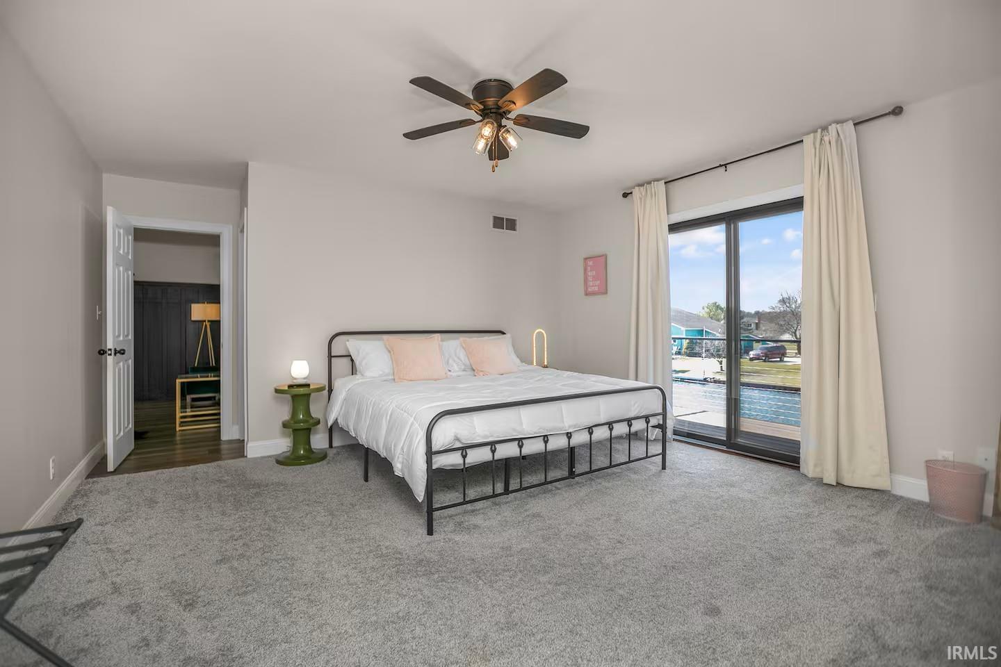 Spacious room featuring light gray walls, plush gray carpeting, and a black ceiling fan with integrated lighting