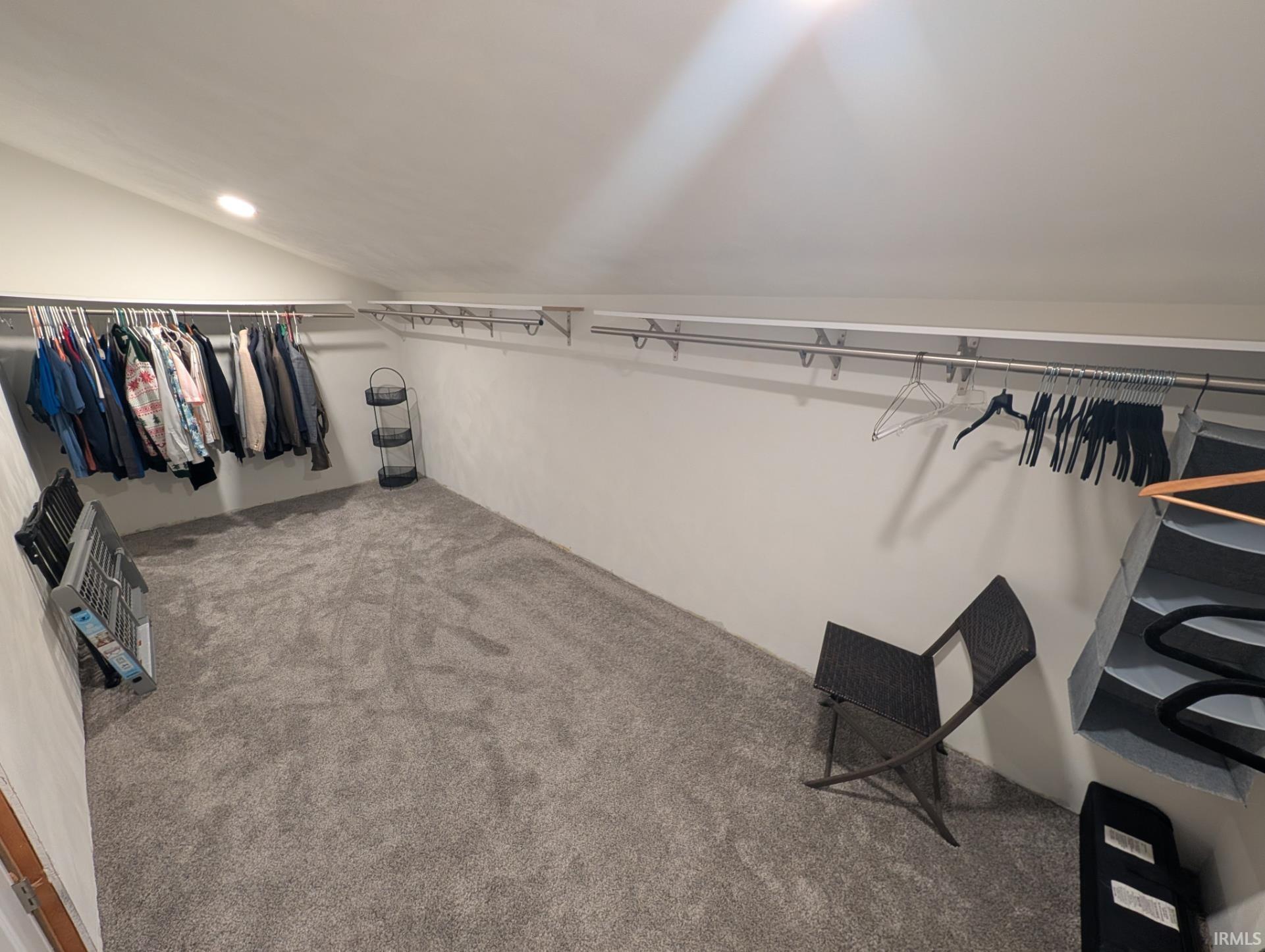 Spacious closet featuring sloped ceilings, recessed lighting, wall-mounted hanging rods, and gray carpeting