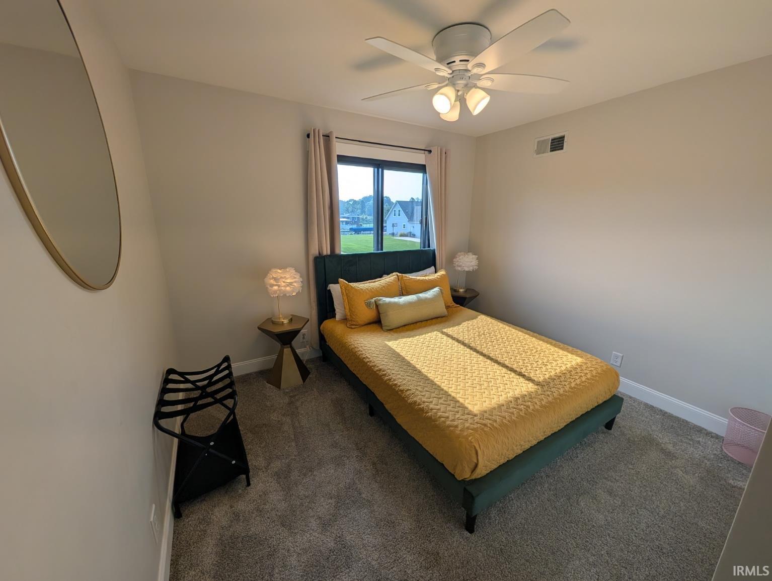 Carpeted bedroom featuring a ceiling fan with integrated lighting, a window with curtains, and neutral wall paint