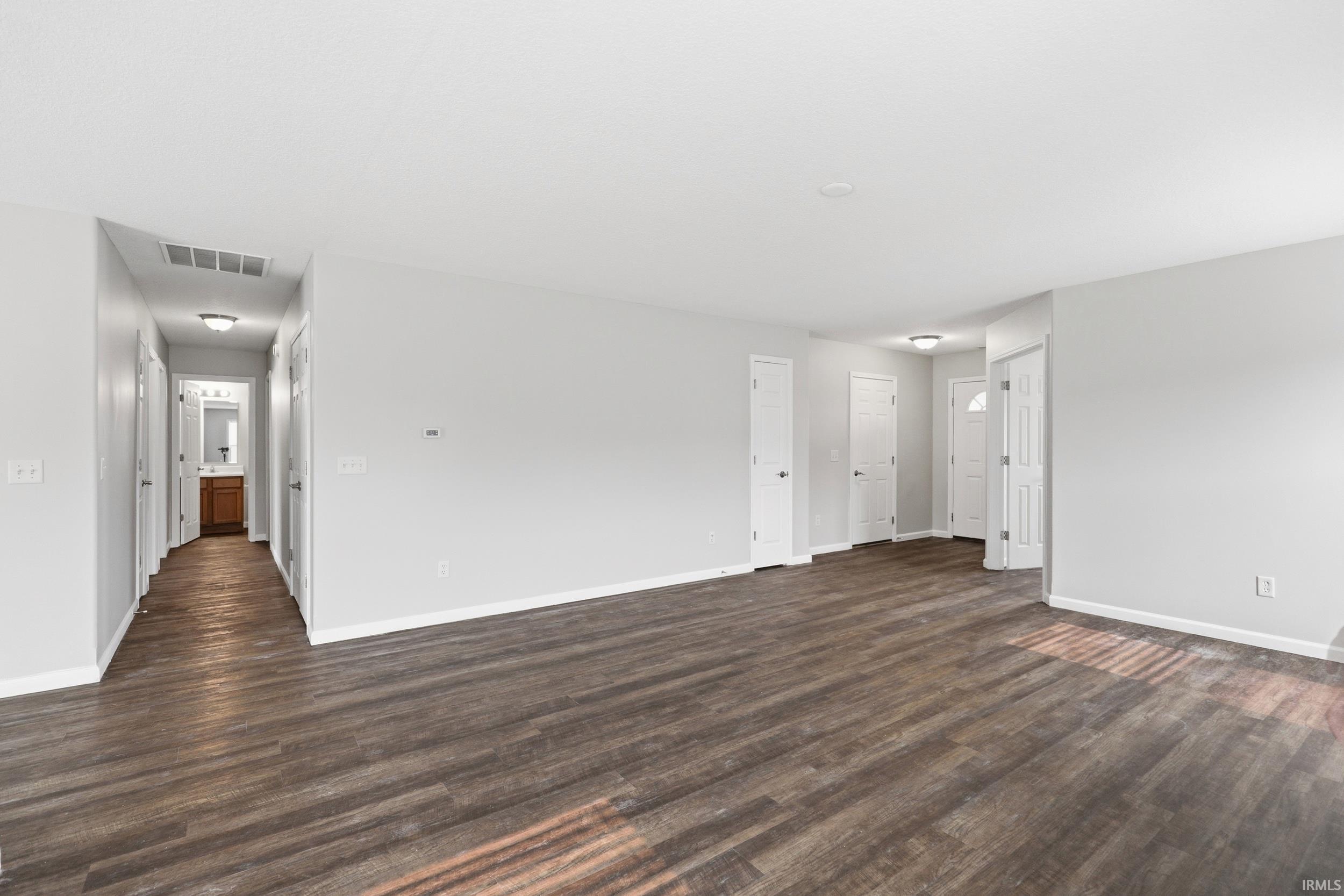Open-concept living space featuring wood-finish flooring, light grey walls, white trim, and a white paneled entry door
