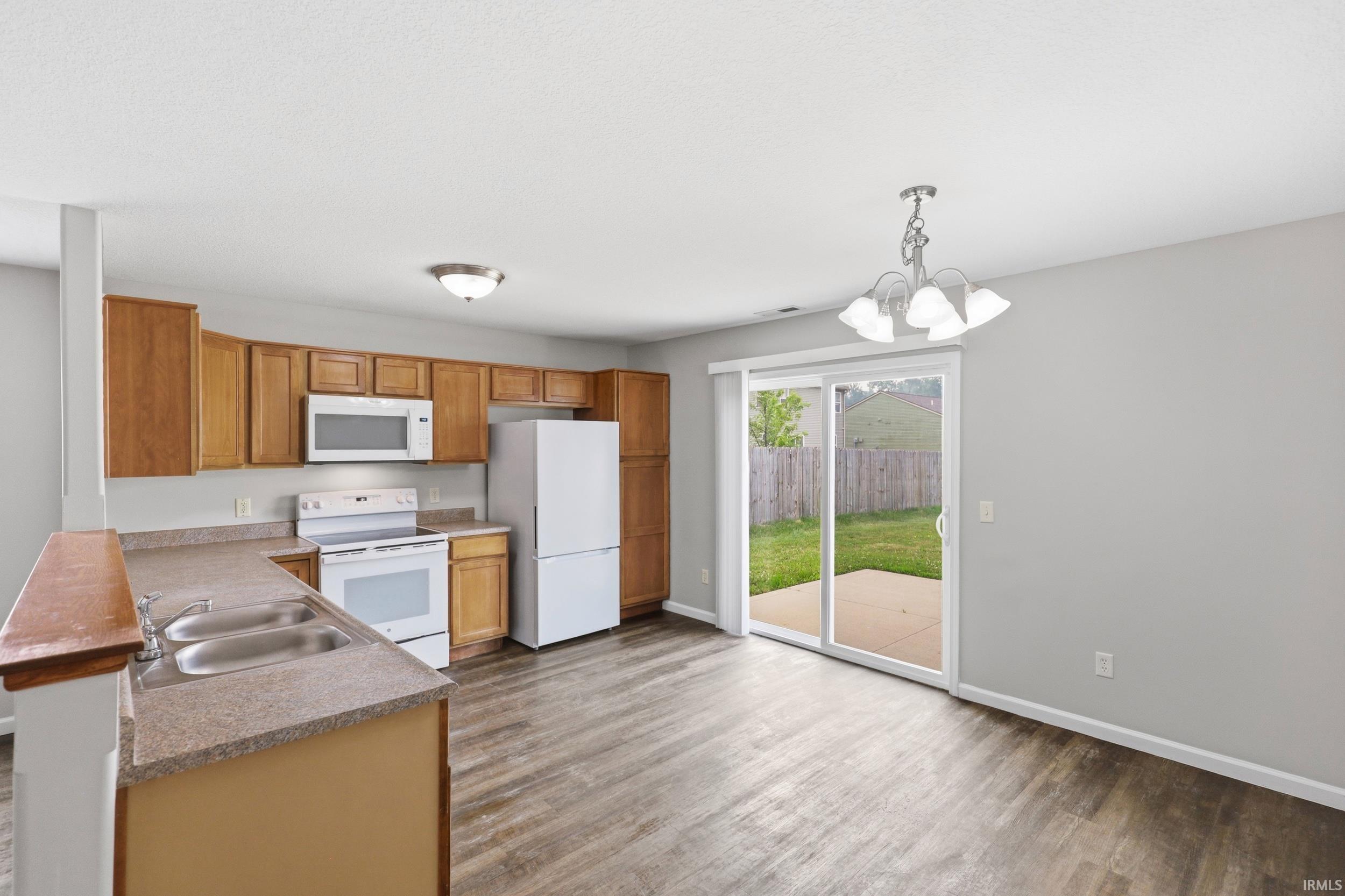 Open-concept kitchen featuring wood cabinetry, white appliances, and a double basin sink