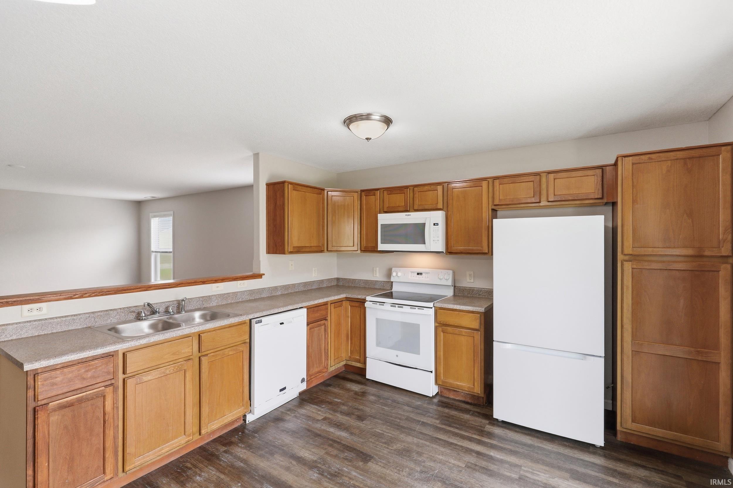 Kitchen featuring wood-finish flooring, light wood cabinetry, and a complete suite of white appliances